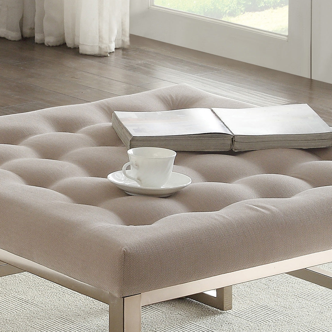 Tufted beige fabric ottoman with a book and teacup for a cozy reading nook