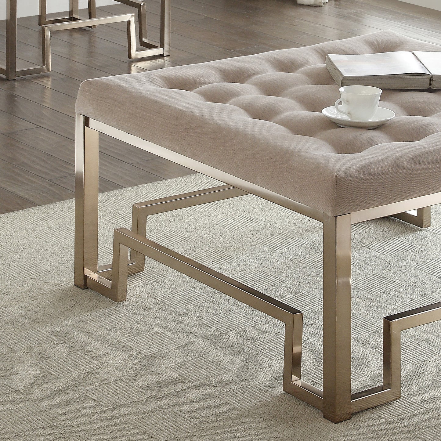 Tufted beige linen ottoman with metallic geometric base and a book and teacup