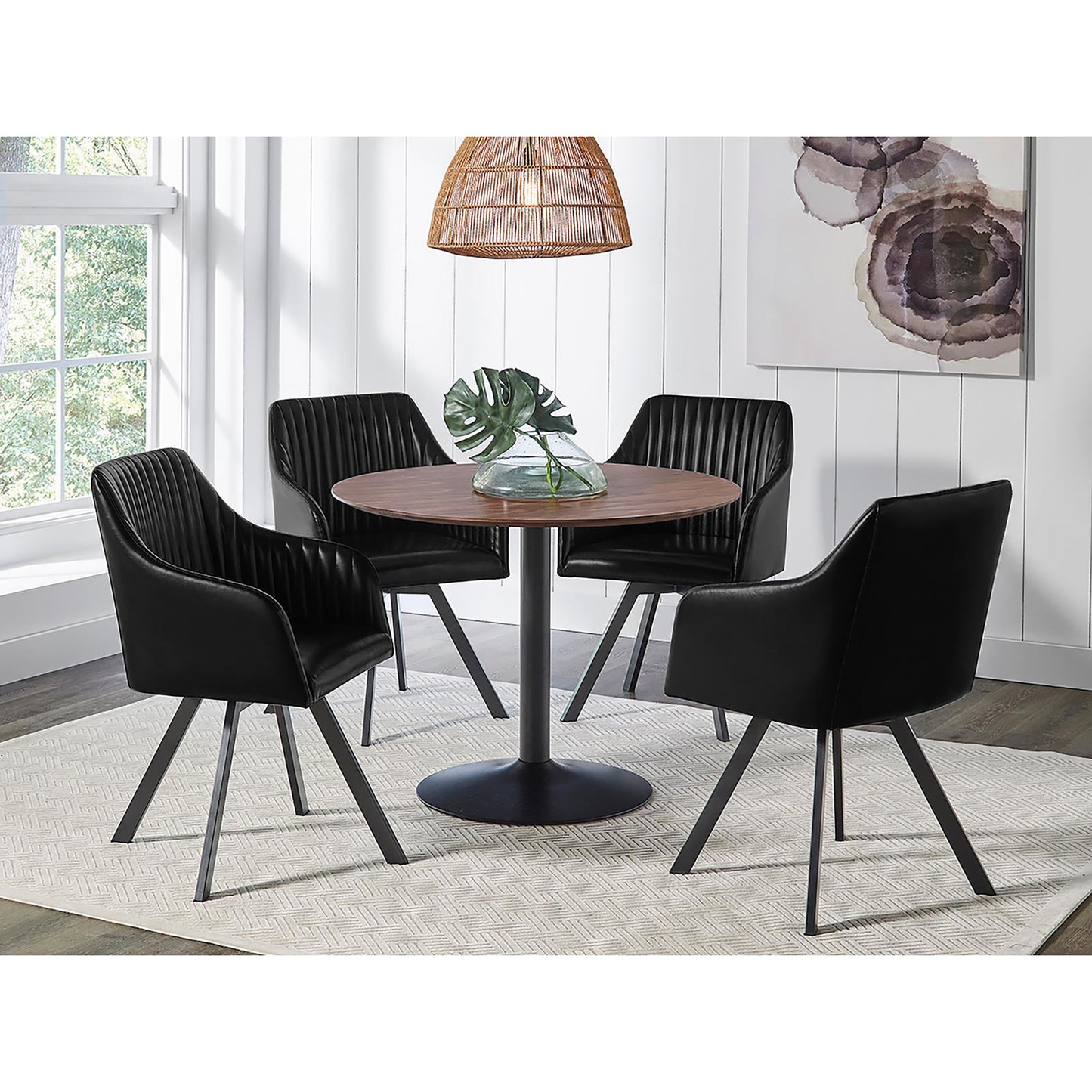 Four black faux leather dining chairs with channel tufting around a round wood dining table