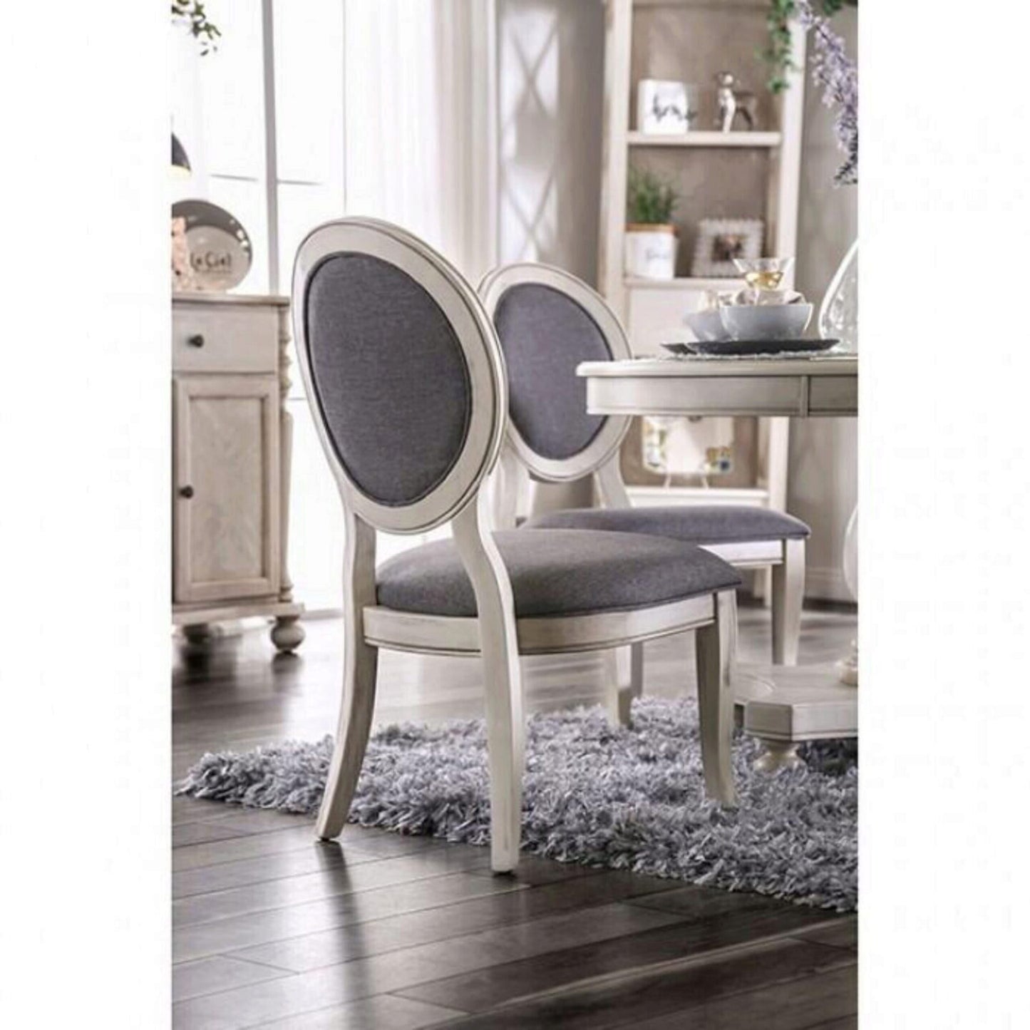 Two upholstered dining chairs with cream ornate frames and grey fabric seats sit on a plush rug
