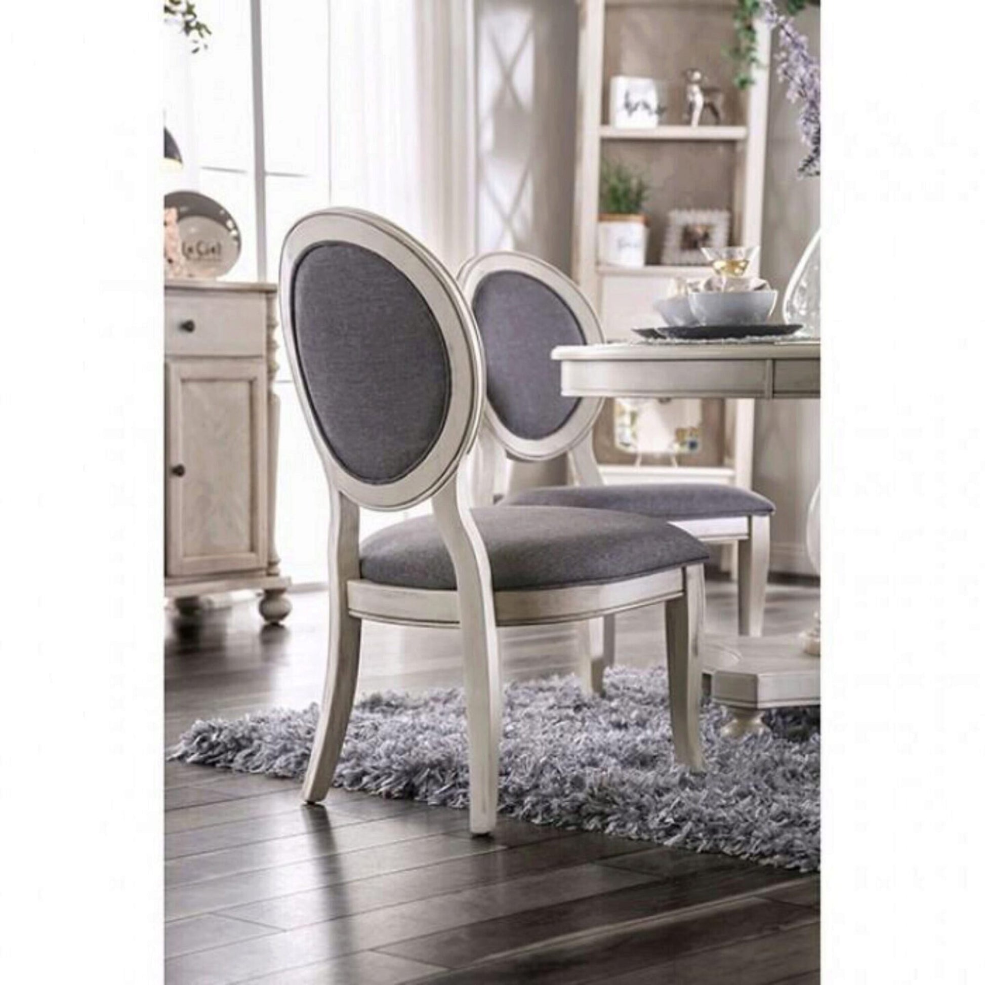 Two upholstered dining chairs with cream ornate frames and grey fabric seats sit on a plush rug