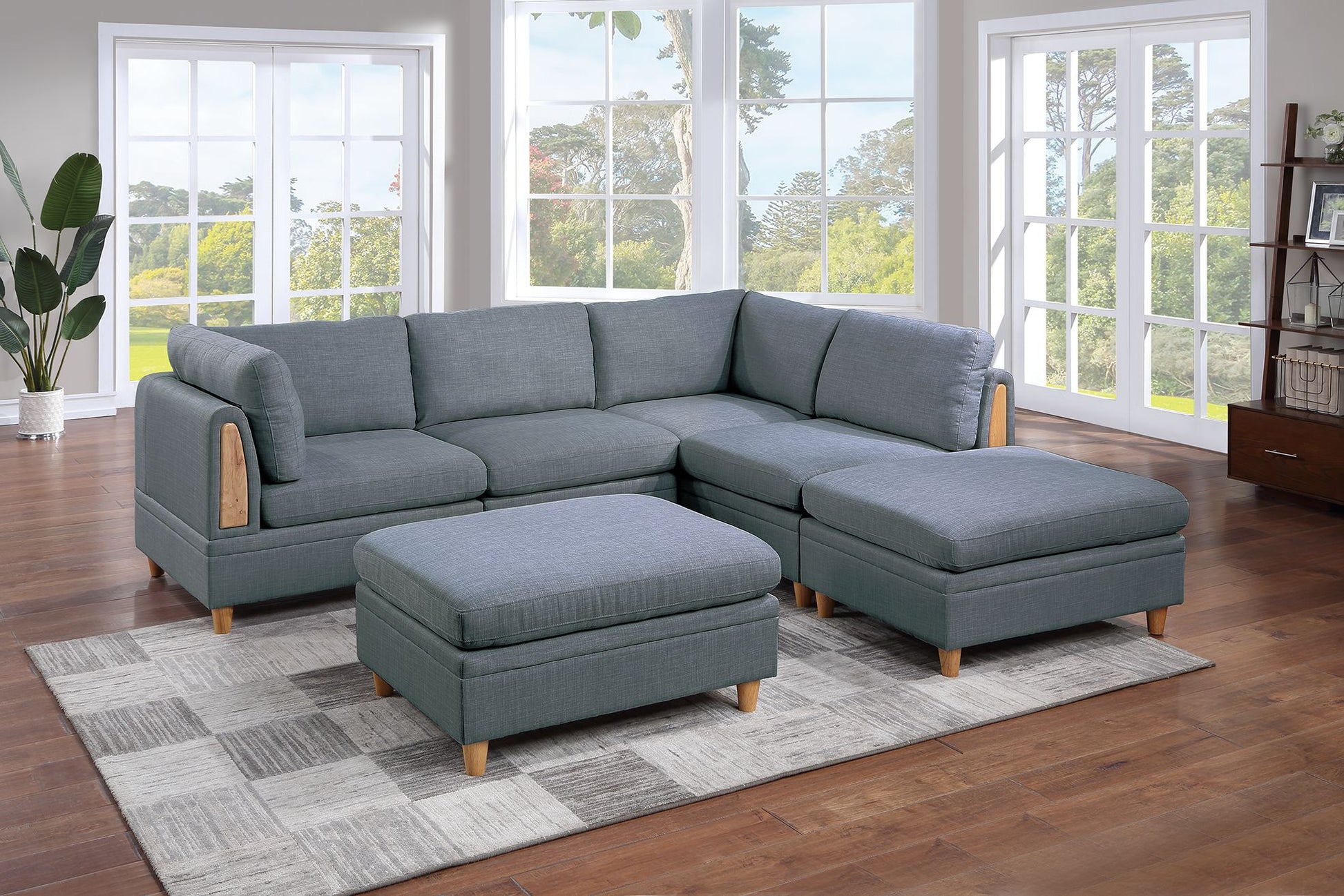 Grey fabric sectional sofa with wooden accents and two matching ottomans on a rug