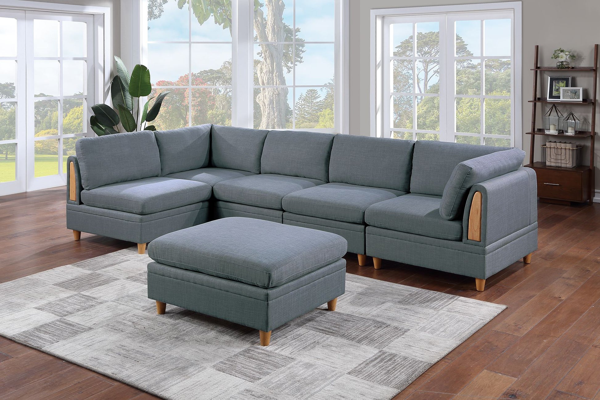 Gray fabric sectional sofa with wooden arm accents and matching ottoman on a geometric rug