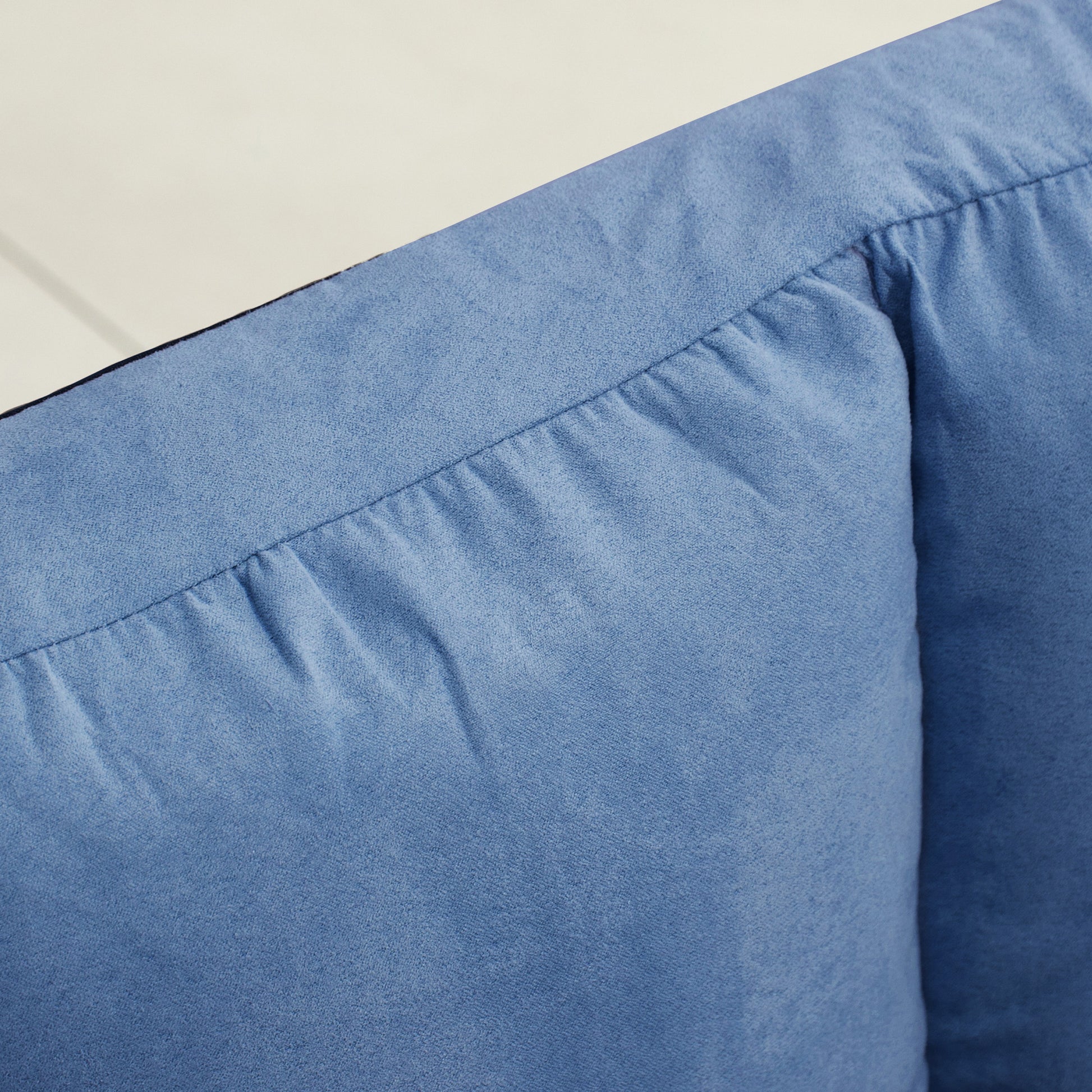 Closeup of light blue denim fabric with detailed stitching and pleats