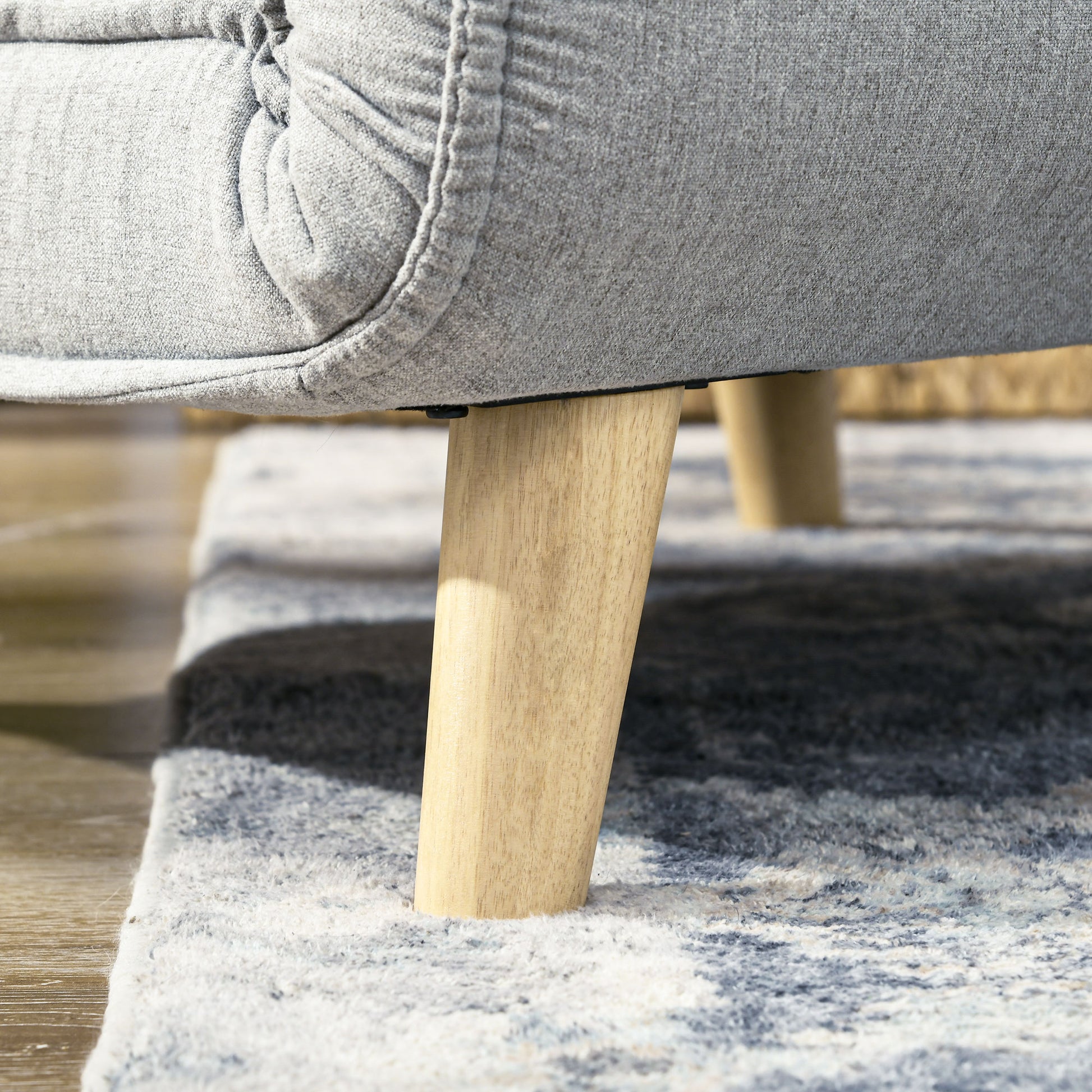 Closeup of plush gray fabric sofa with tapered wooden leg on patterned rug