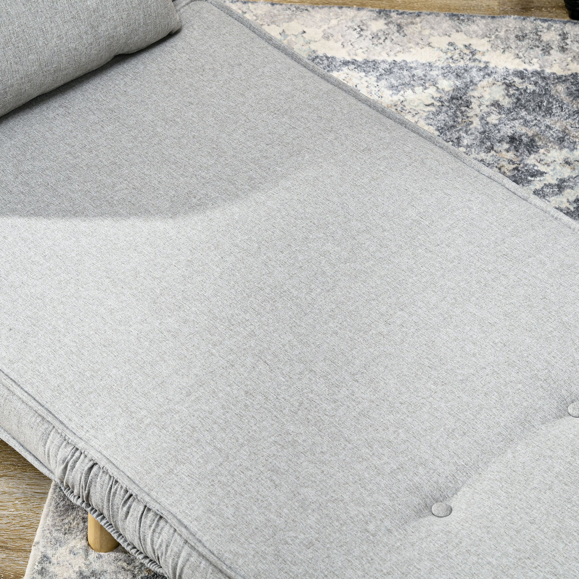 Closeup of a light gray fabric chaise lounge with tufted buttons and a ruffled skirt