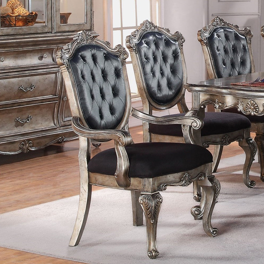 Ornate silver dining chairs with black tufted upholstery and carved details