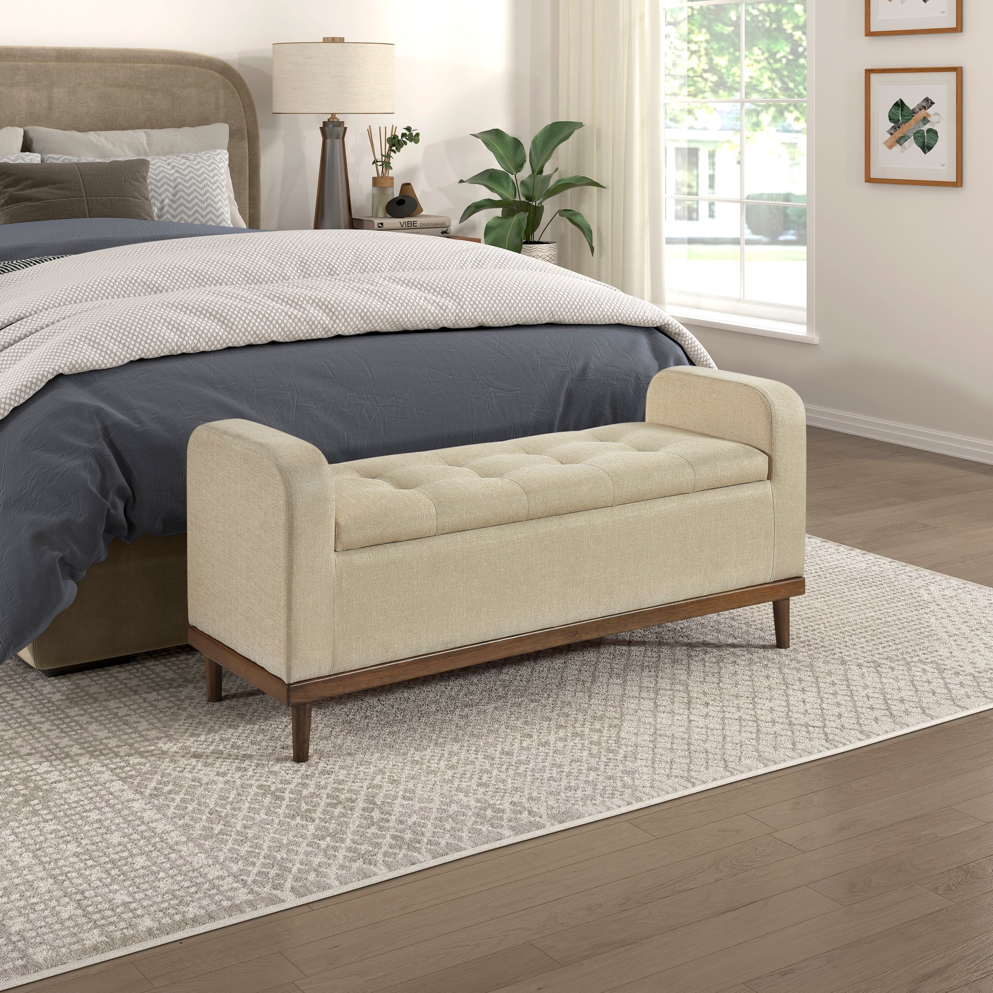 Beige tufted storage bench with dark wood legs in a bedroom setting