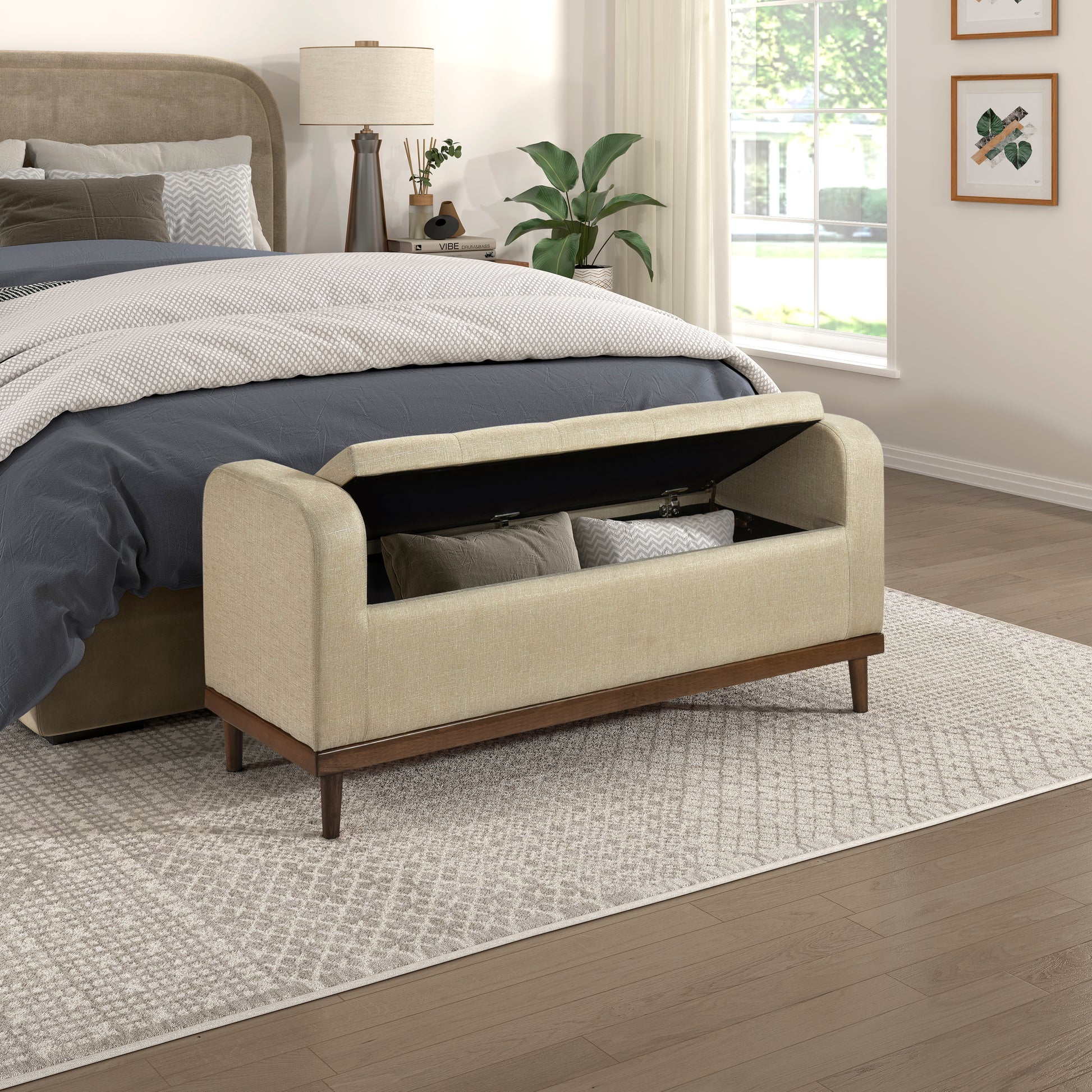 Cream upholstered storage bench with dark wood legs and open lid revealing pillows