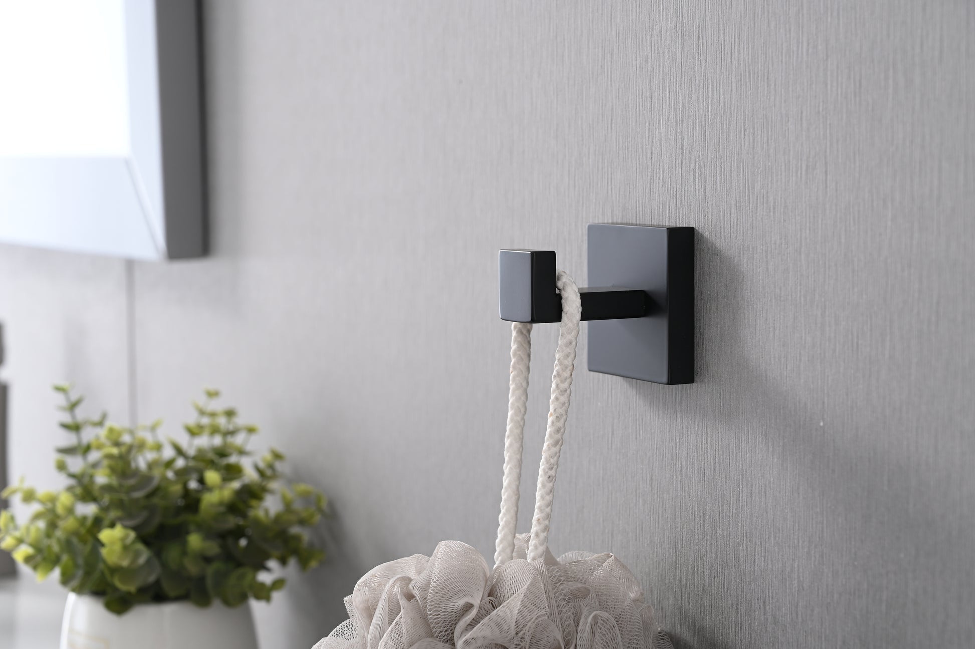 Modern matte black square bathroom hook holding a white rope bath pouf