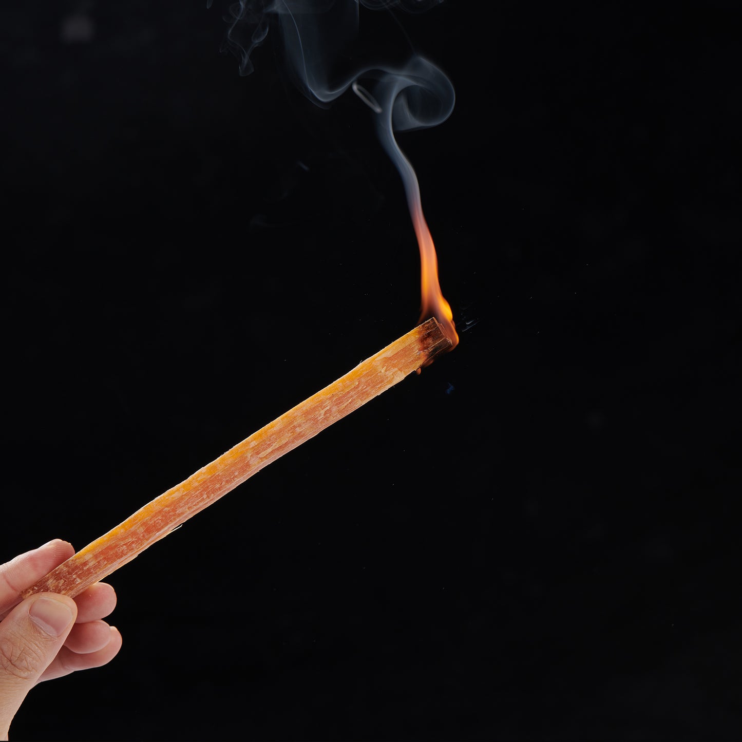 Hand holding burning palo santo stick with wisps of smoke for smudging