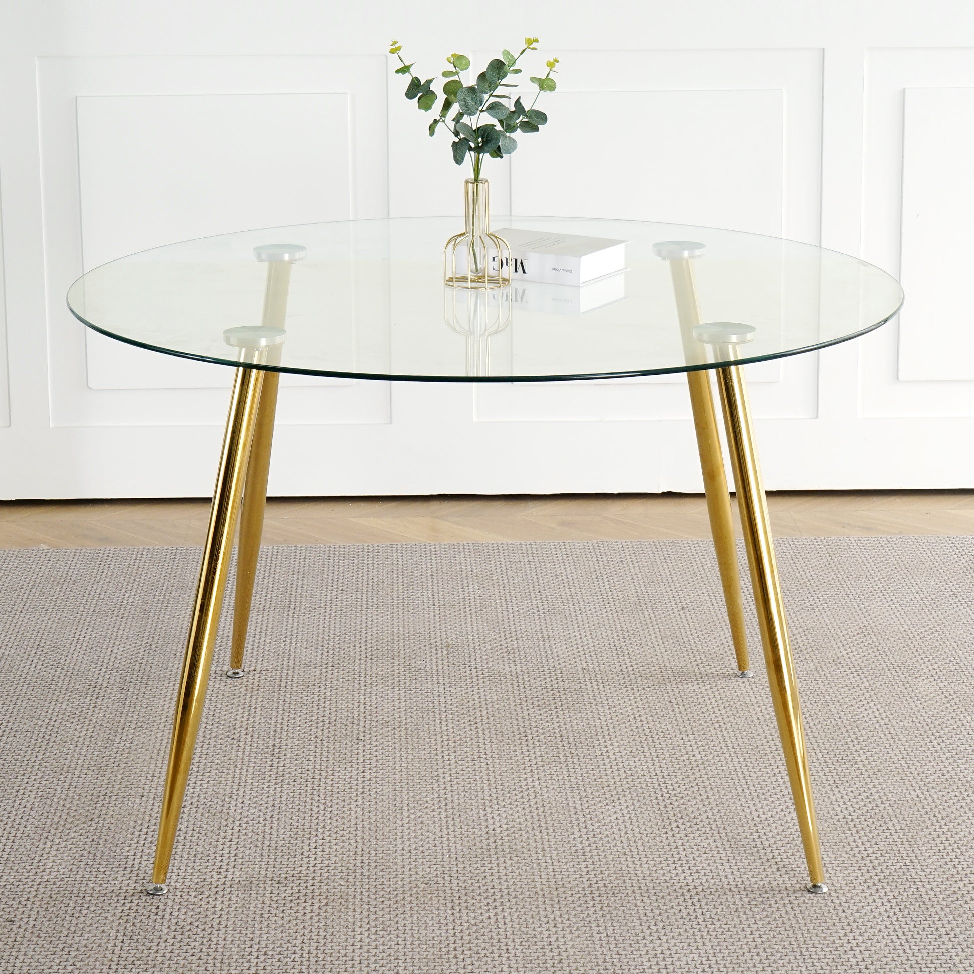Round glass dining table with gold tapered legs and a small plant