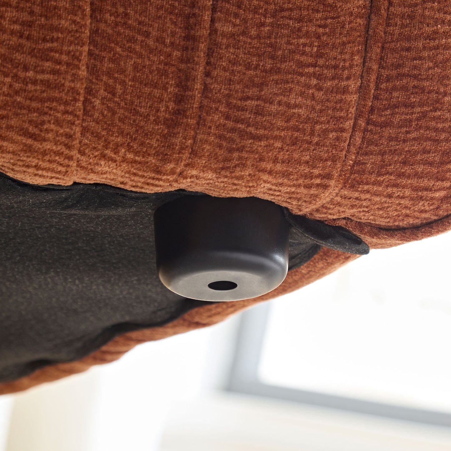 Closeup of a brown textured fabric on a couch with a black furniture leg visible