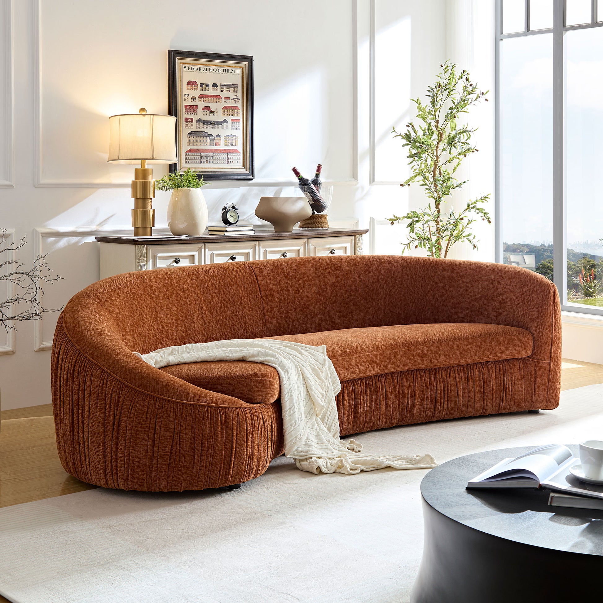 Curved sectional sofa in burnt orange velvet with pleated detailing featuring a cream throw