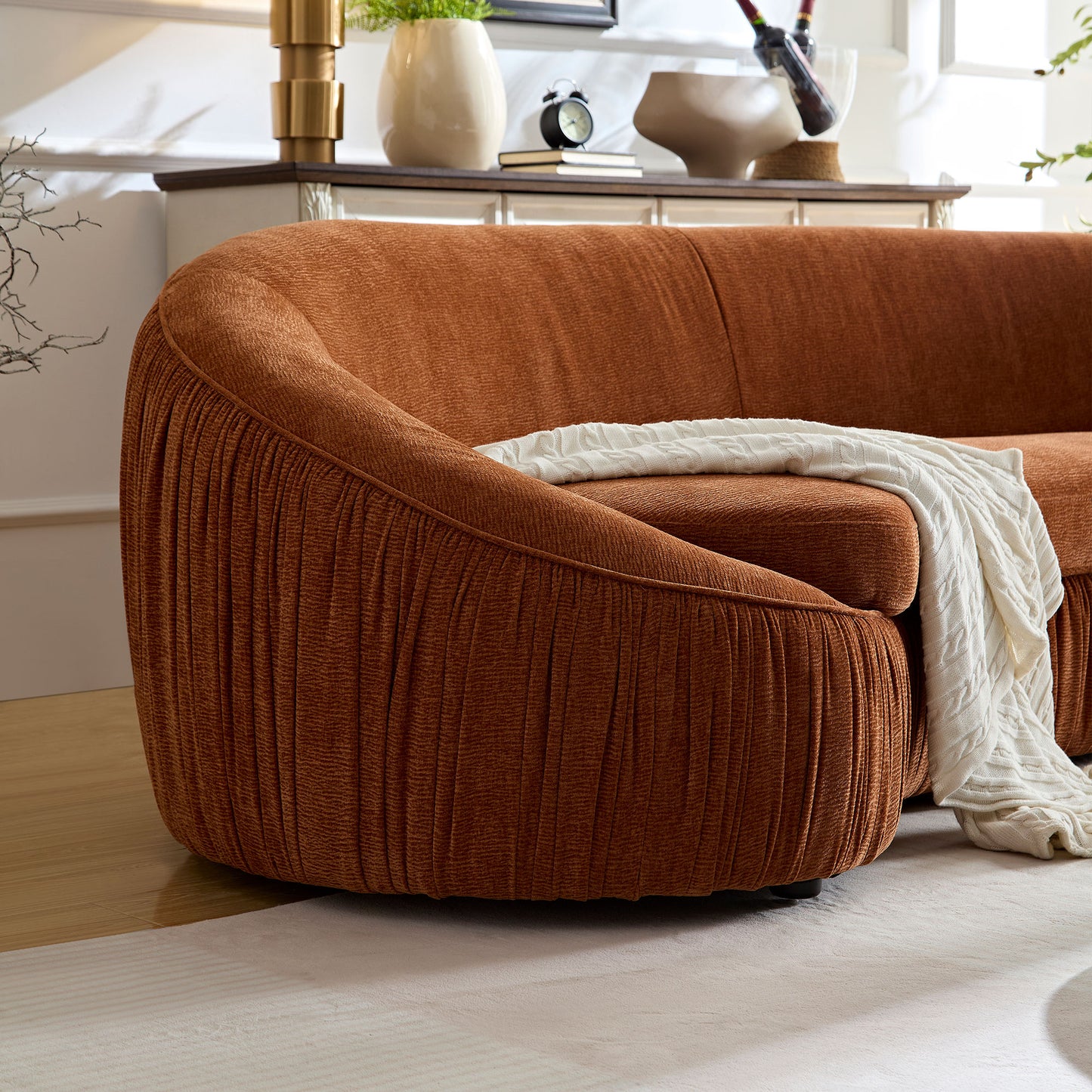 Curved rustorange boucle sofa with pleated base and draped white throw blanket