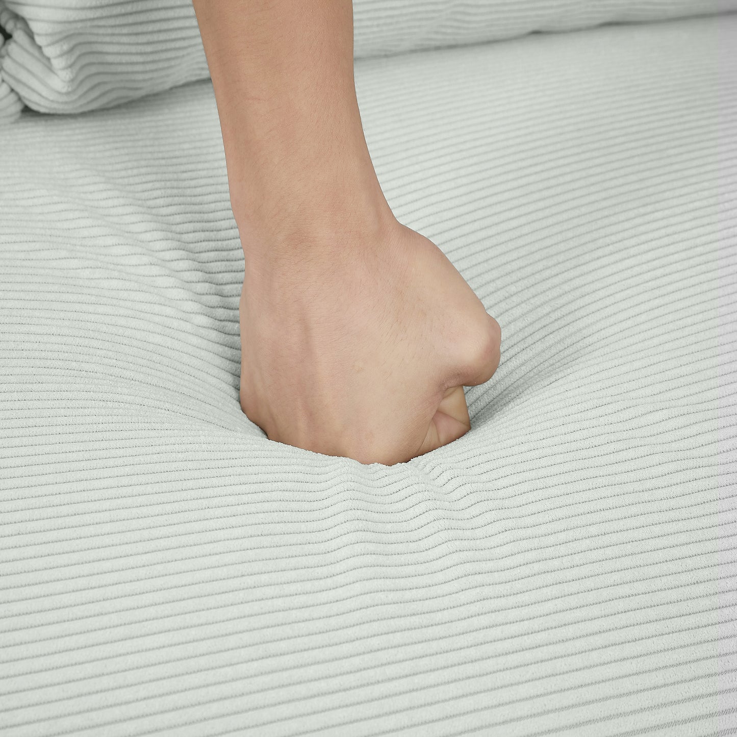 Closeup of a fist pressing into soft light gray corduroy fabric