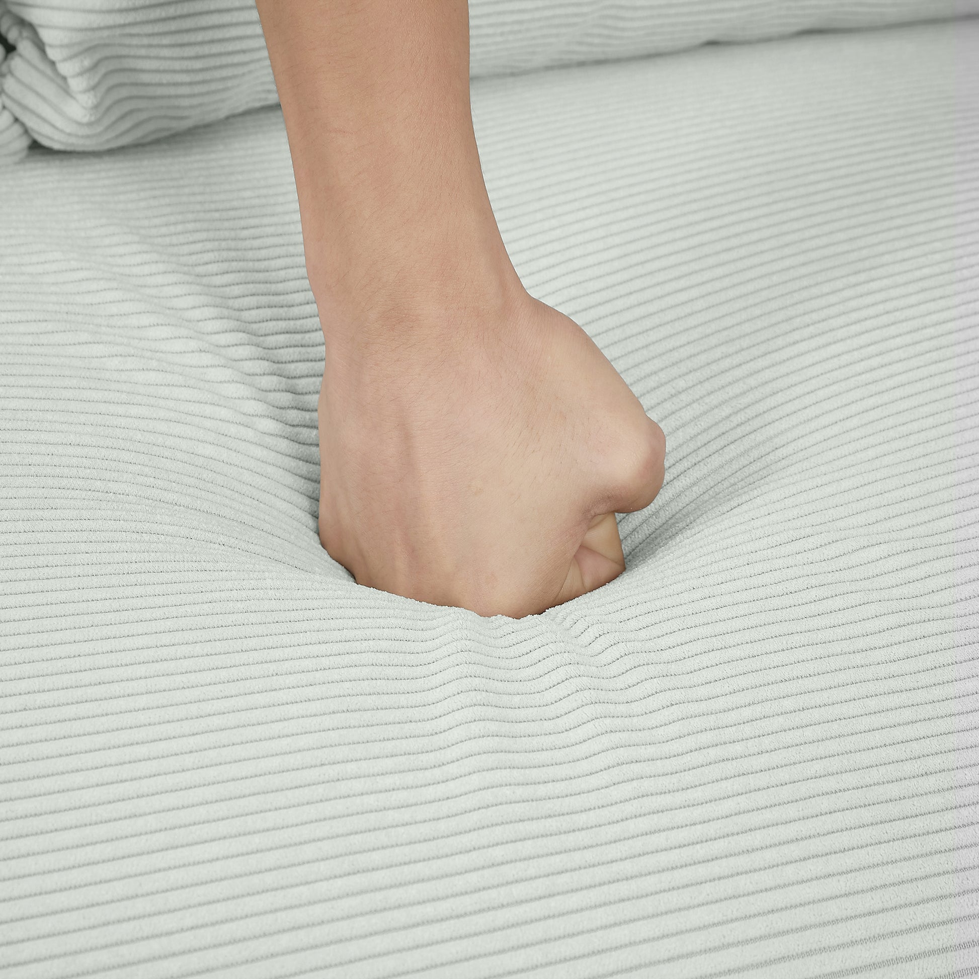 Closeup of a fist pressing into soft light gray corduroy fabric