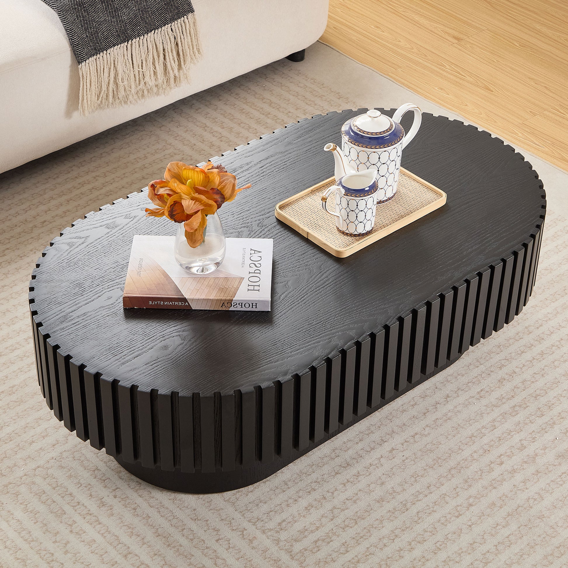 Dark wood oval coffee table with ridged detailing featuring a book and vase with flowers