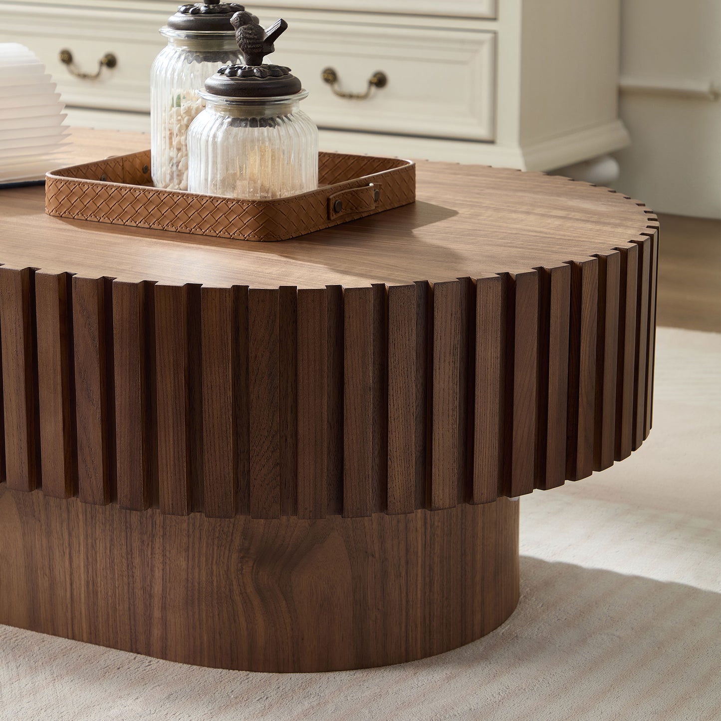 Round fluted walnut coffee table with decorative glass jars on a woven tray