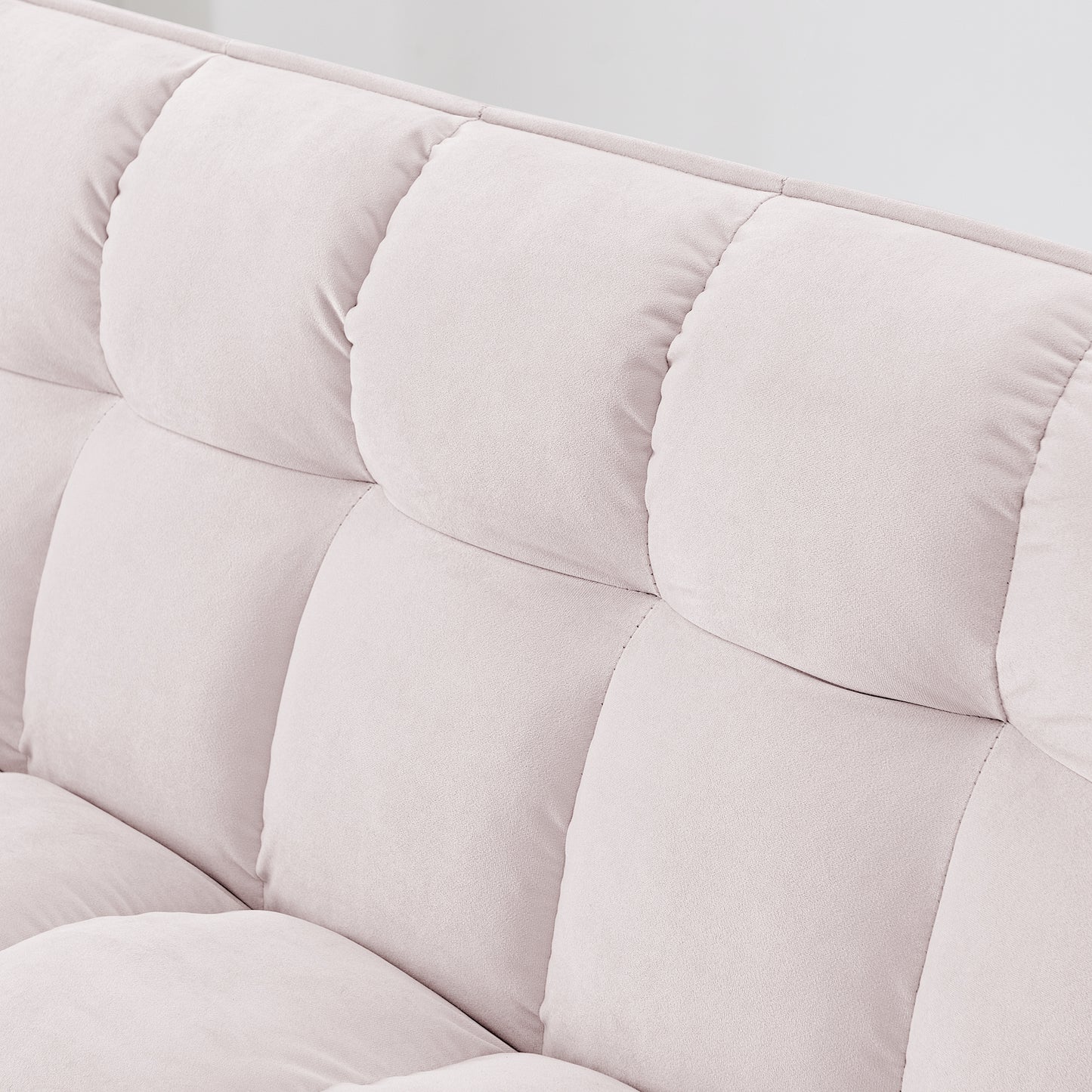 Closeup of a plush light pink velvet sofa with tufted back cushions