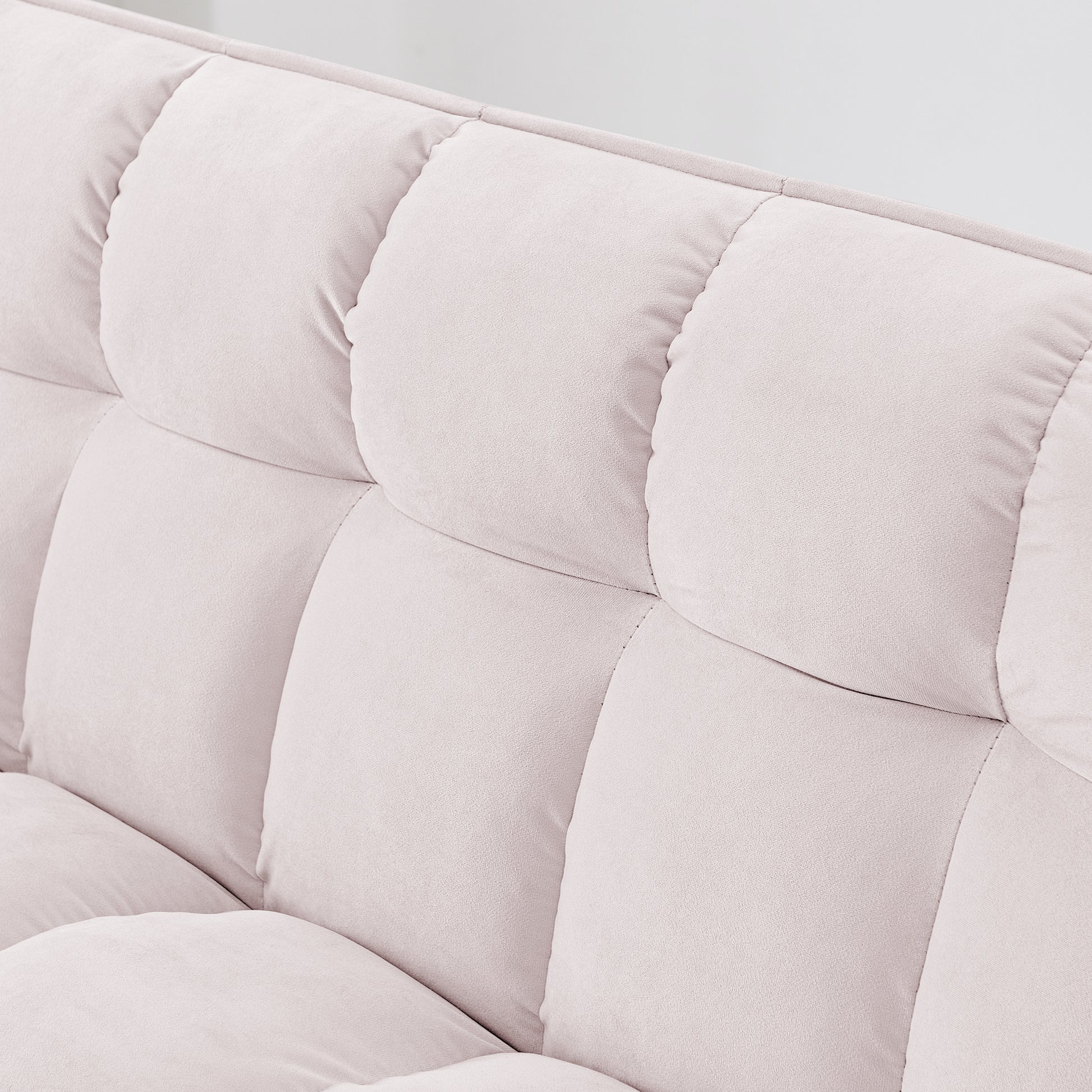 Closeup of a plush light pink velvet sofa with tufted back cushions