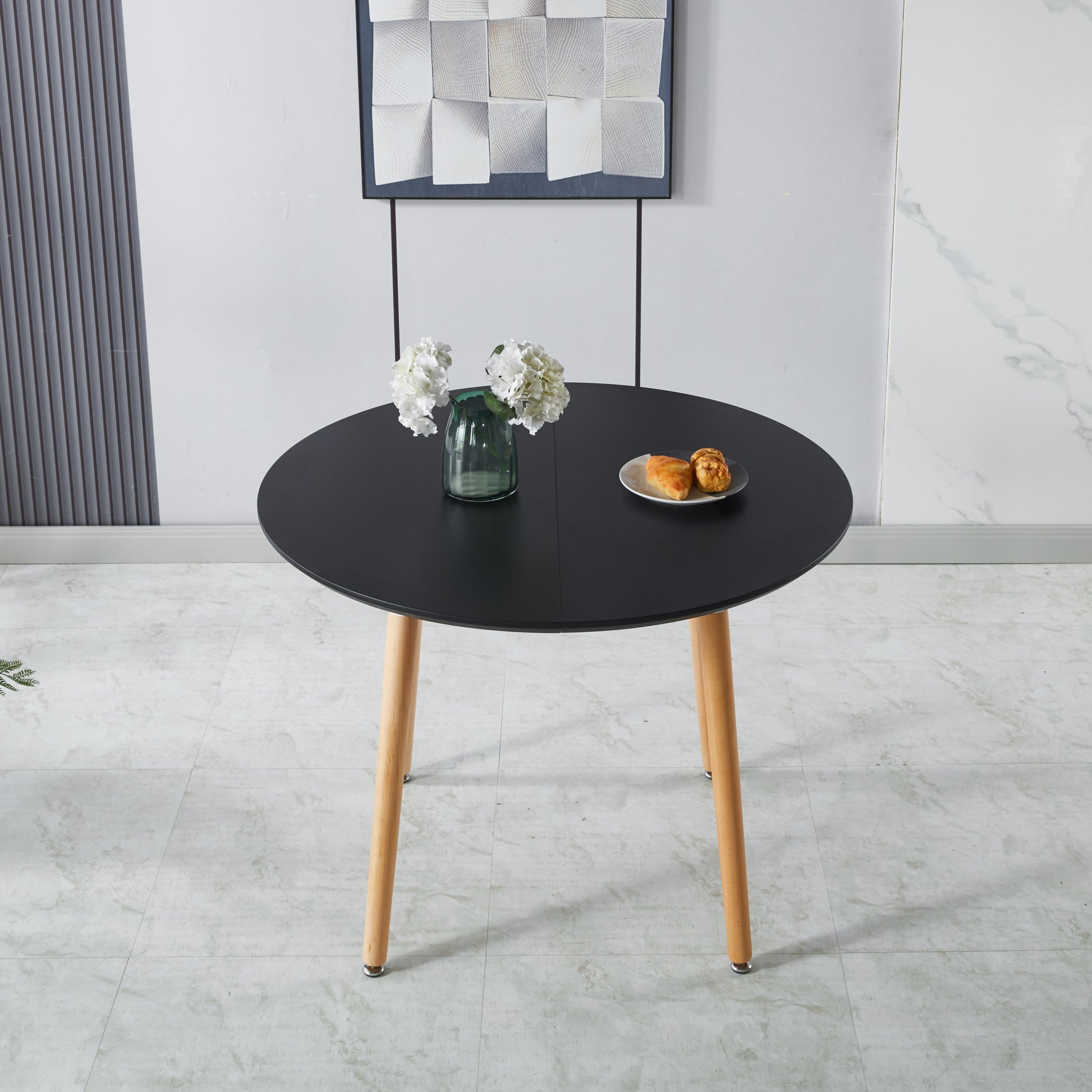 Black round dining table with light wood legs and two pastries on a plate