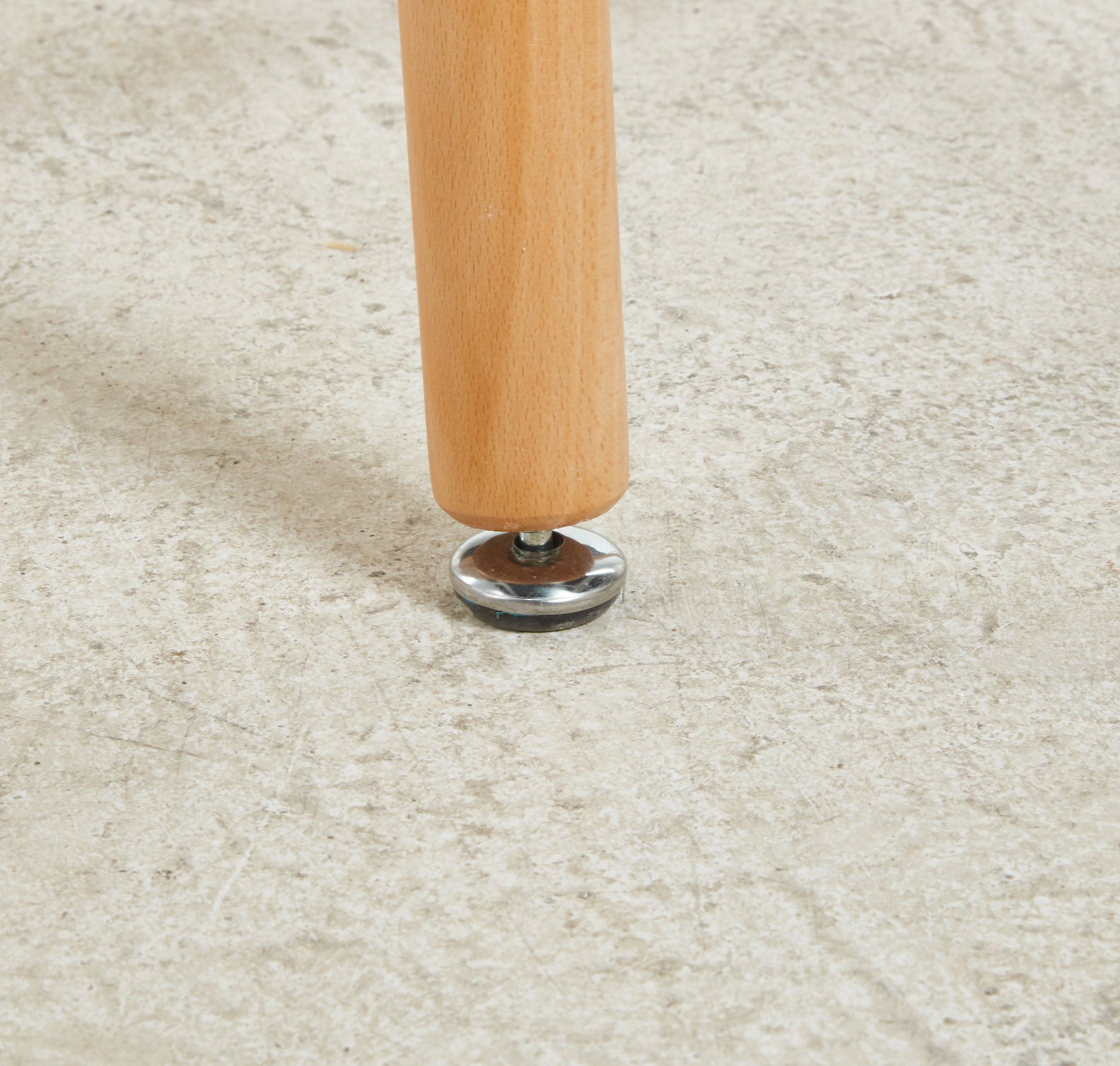 Detail of a light wood furniture leg with a metal adjustable foot on a concrete floor