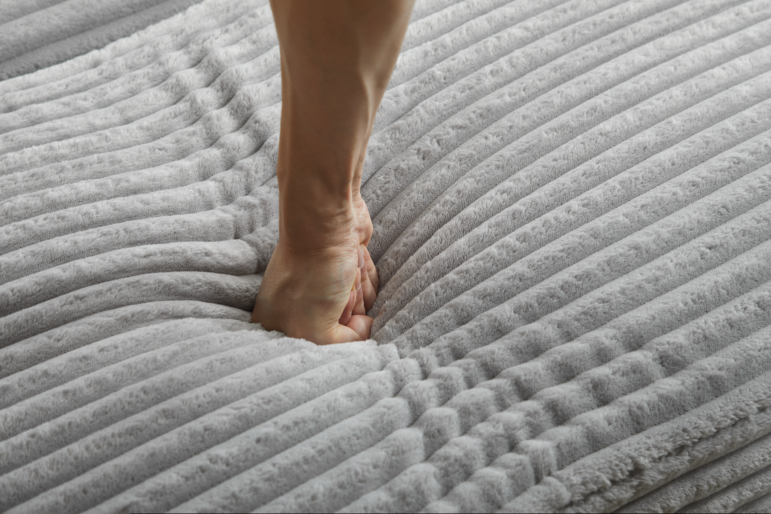 Closeup of a hand pressing into a plush ribbed grey blanket demonstrating softness