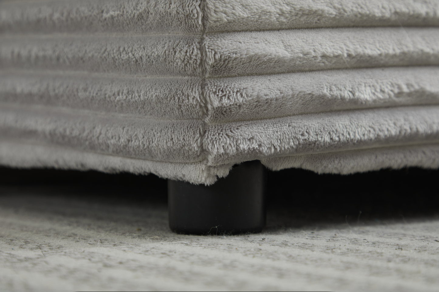 Closeup of plush grey corduroy fabric sofa corner with dark support leg