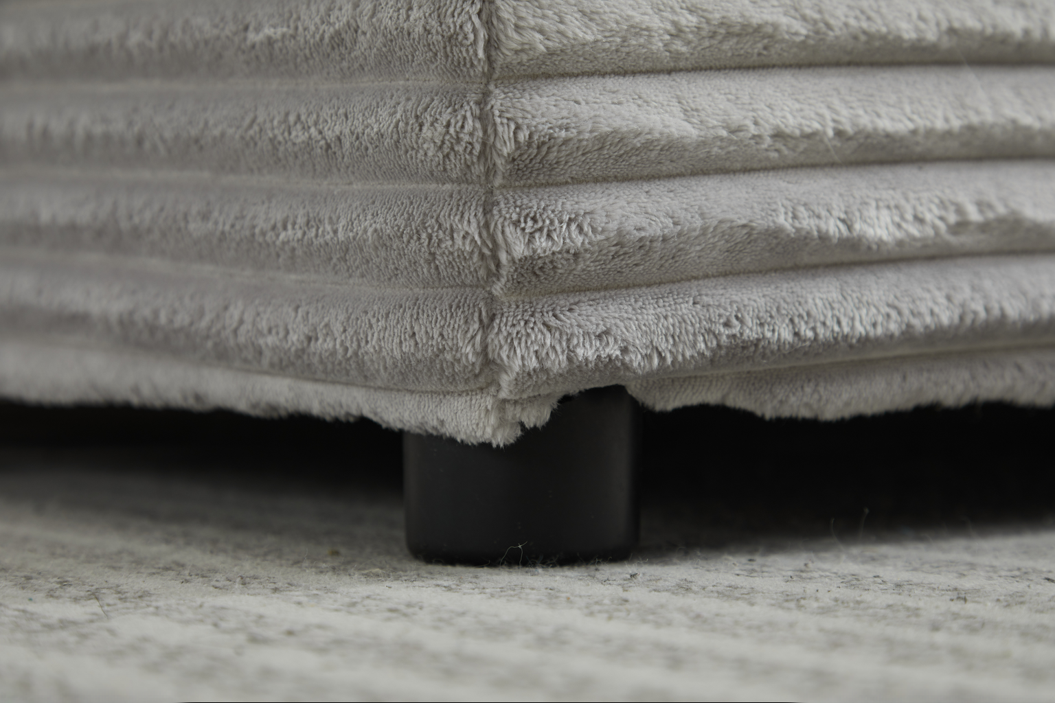 Closeup of plush grey corduroy fabric sofa corner with dark support leg