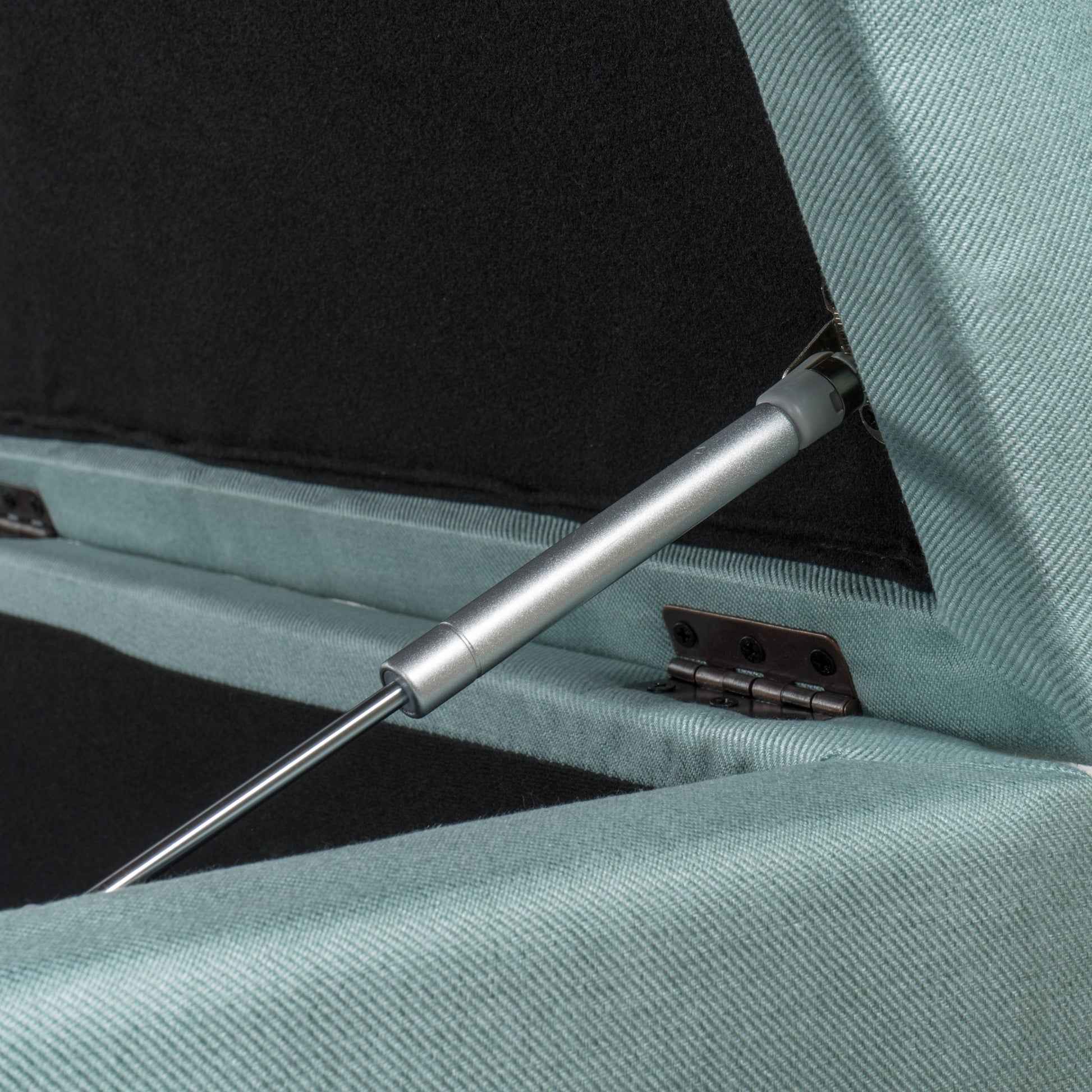 Closeup of a teal upholstered storage ottoman lid support mechanism with gas strut