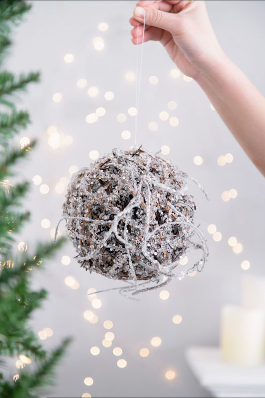 Hand holding a textured pinecone Christmas ornament with glitter and twine details