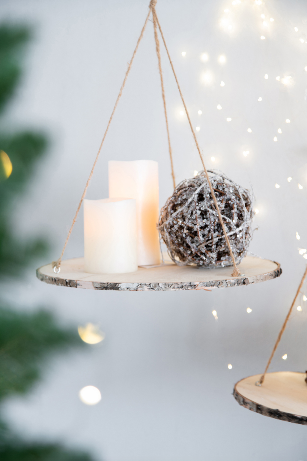 Hanging wooden slice shelf with white pillar candles and a sparkly orb ornament