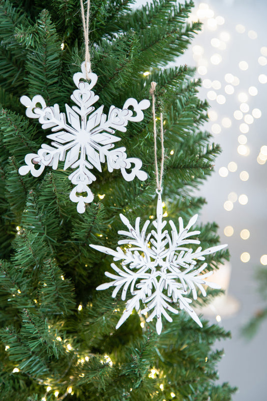 Two white snowflake ornaments hang on a green Christmas tree with bokeh lights