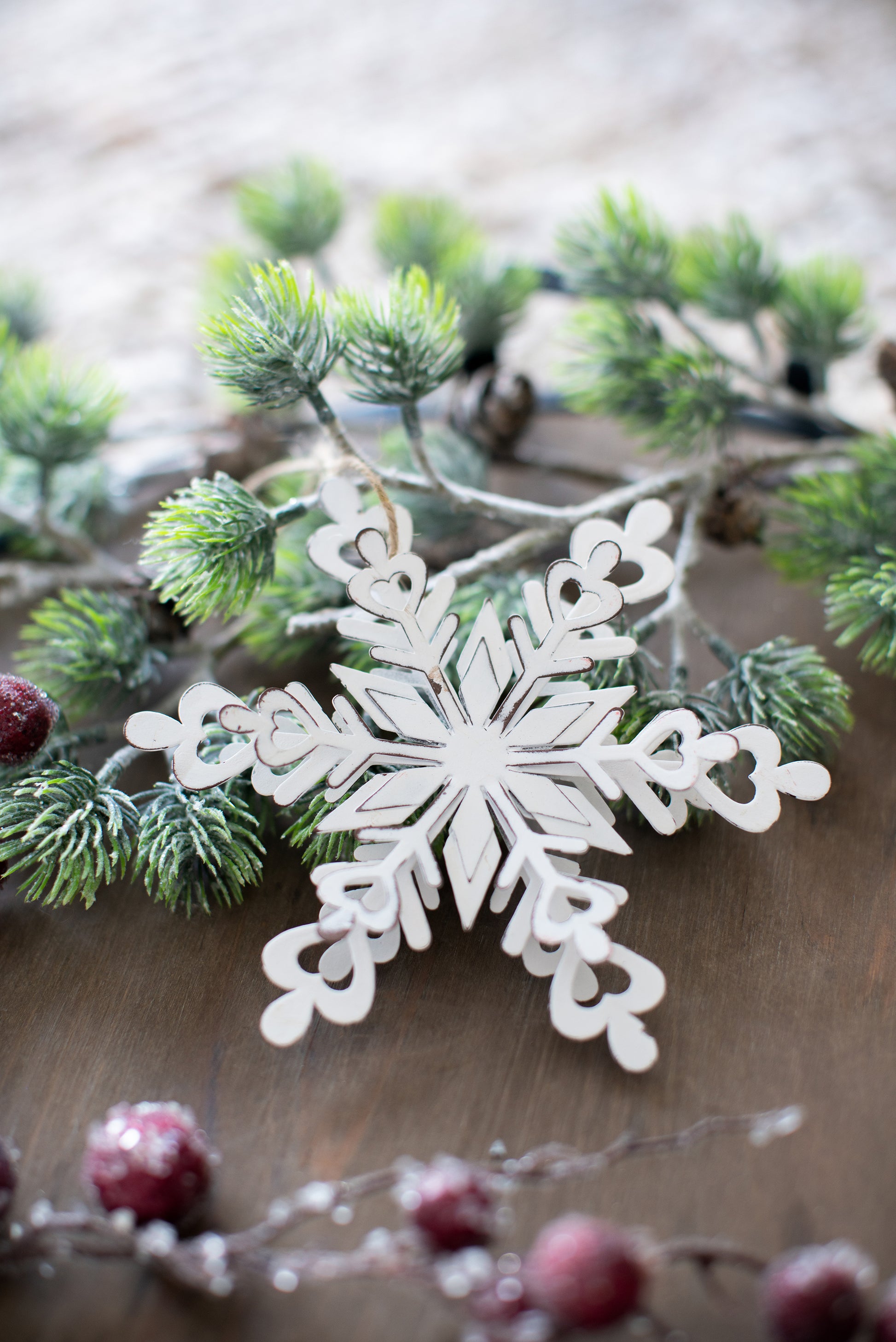 White wooden snowflake ornament with rustic distressed edges on pine branch
