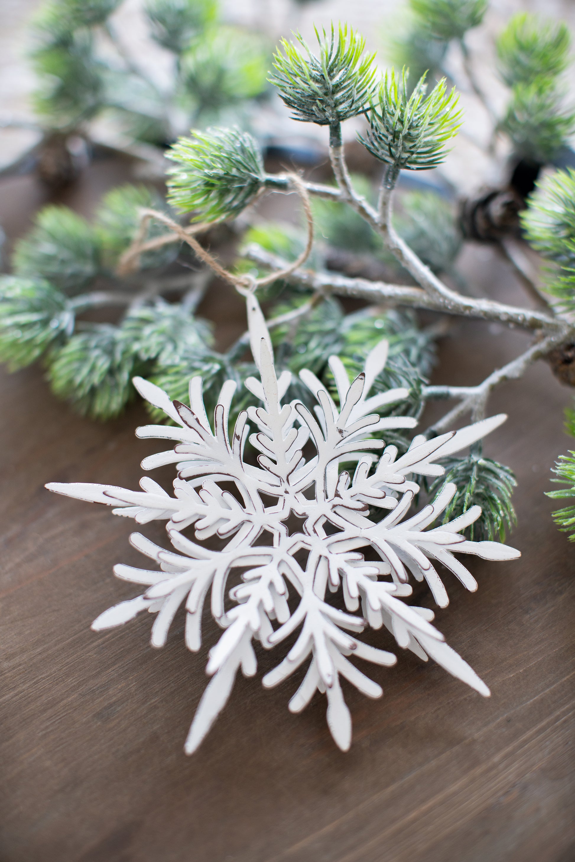Rustic white metal snowflake ornament with distressed brown edges hanging from pine branch