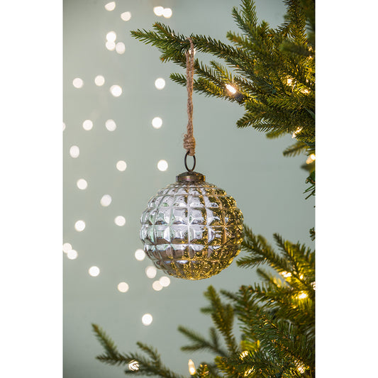 Textured silver glass Christmas ornament hanging on a festive tree branch