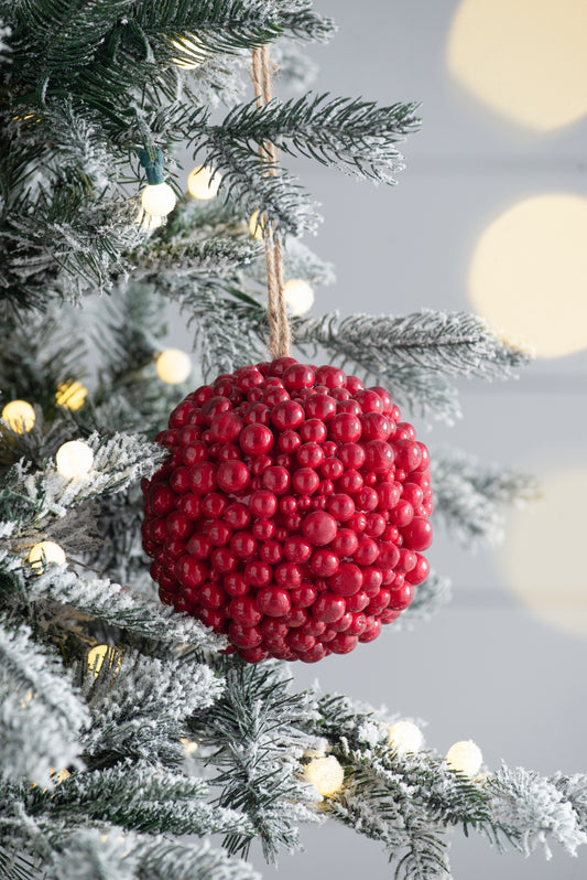 Red berry cluster Christmas ornament on a flocked pine tree branch with fairy lights
