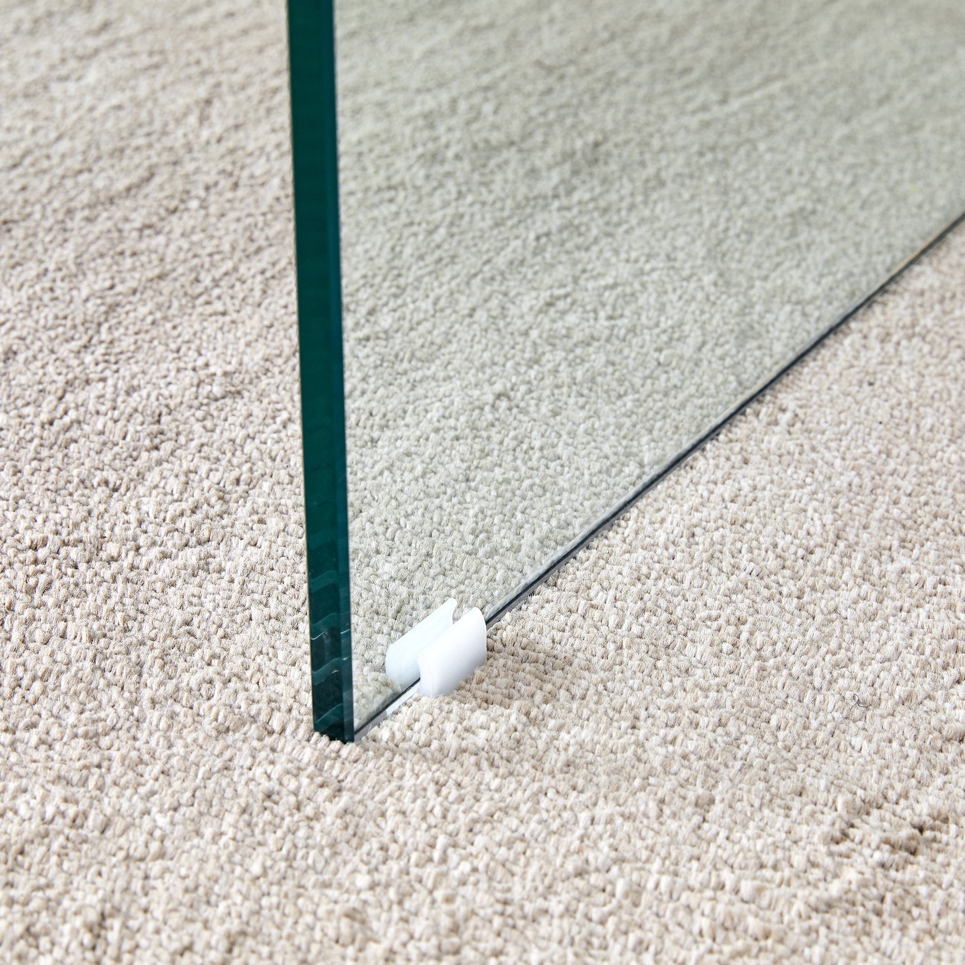 Closeup of a clear glass panel with a white floor protector on a textured beige carpet