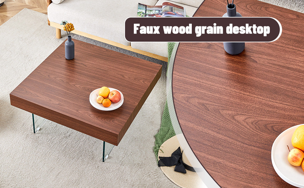 Square faux wood grain coffee table with clear glass legs holding fruit and a vase