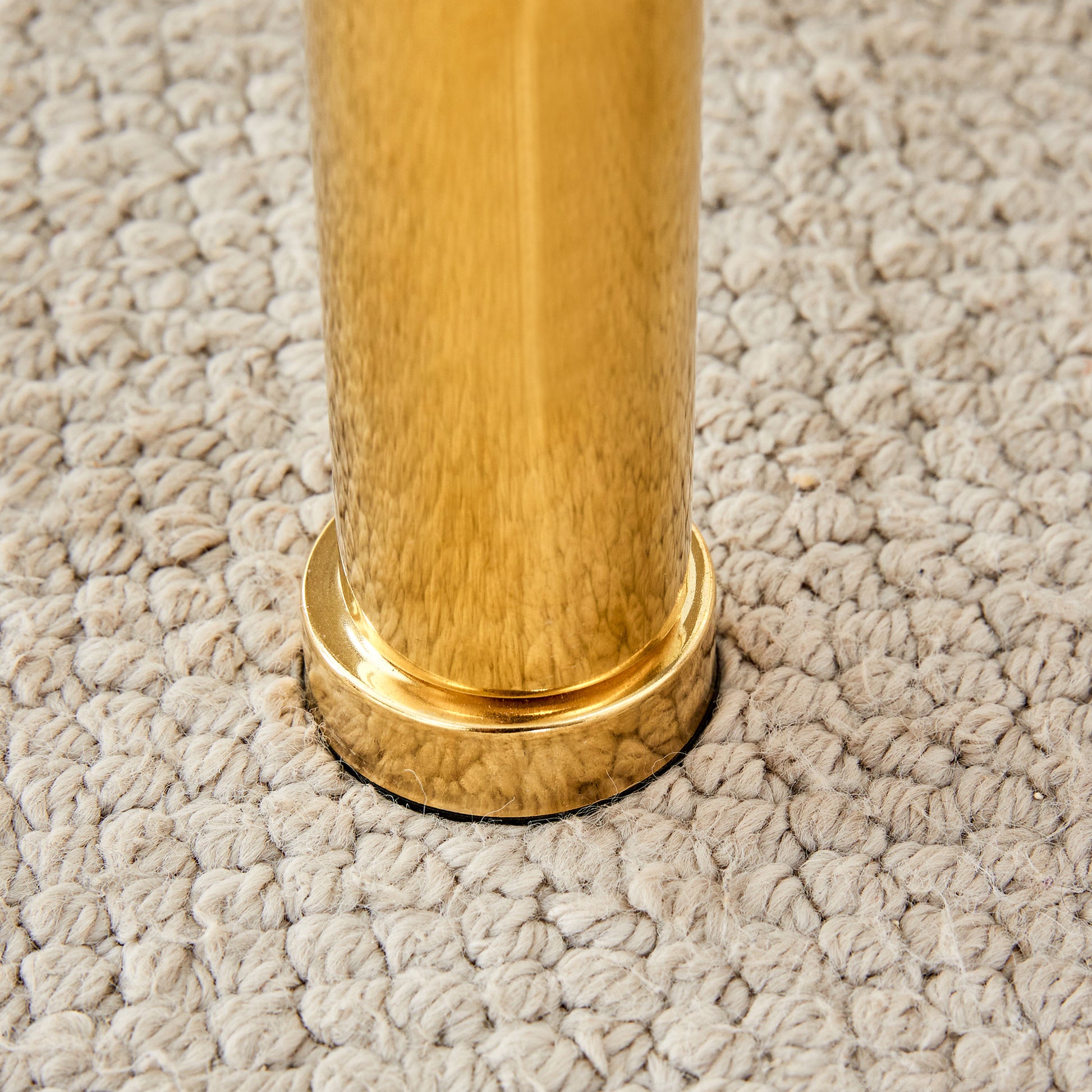 A closeup of a gold metal furniture leg resting on a textured beige rug
