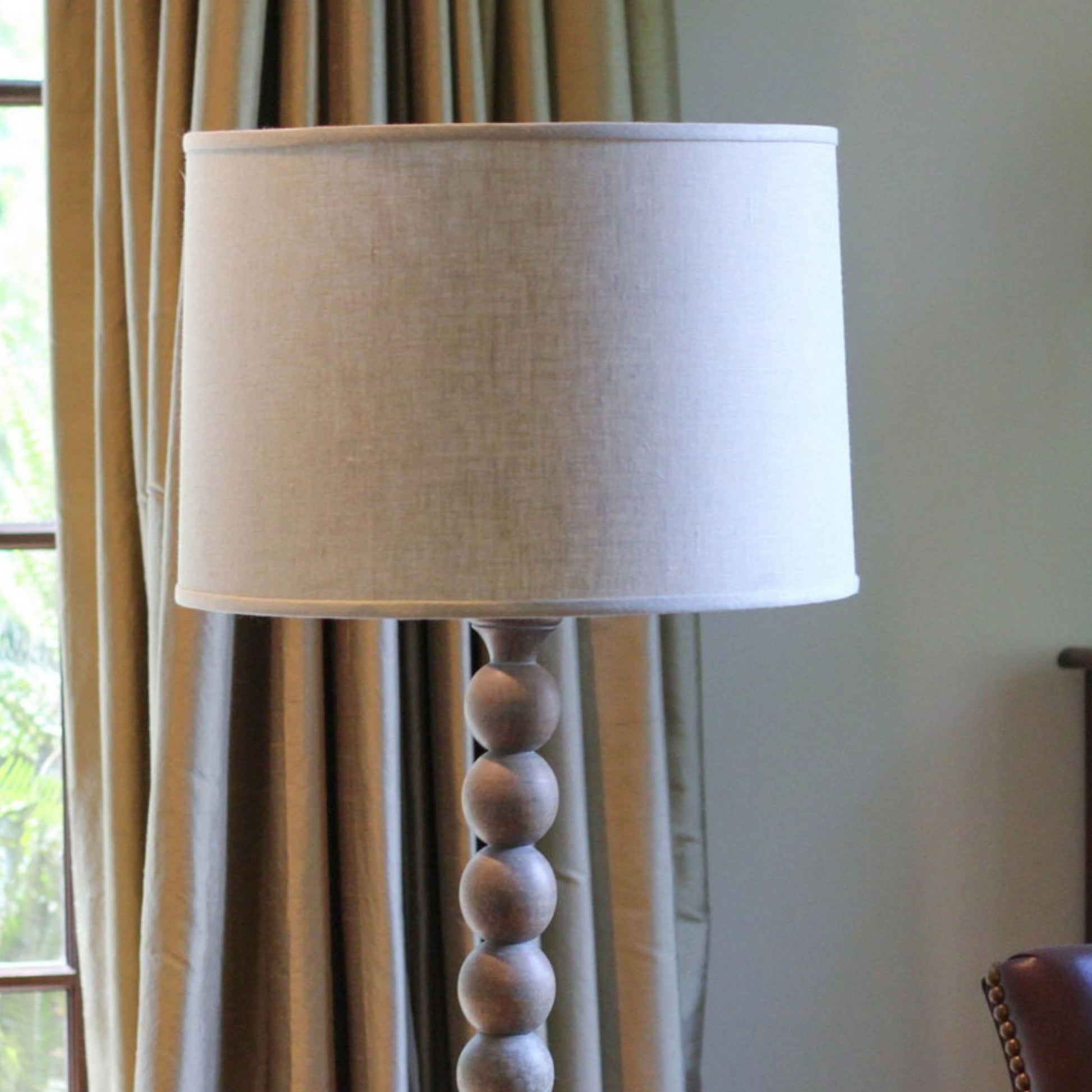 Cream linen drum lampshade on a wooden beaded floor lamp with a natural finish