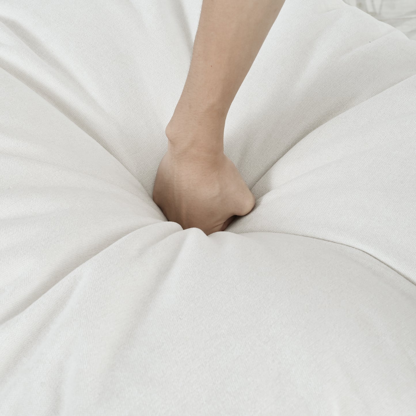 Hand pressing into a soft white fabric cushion highlighting its plush texture