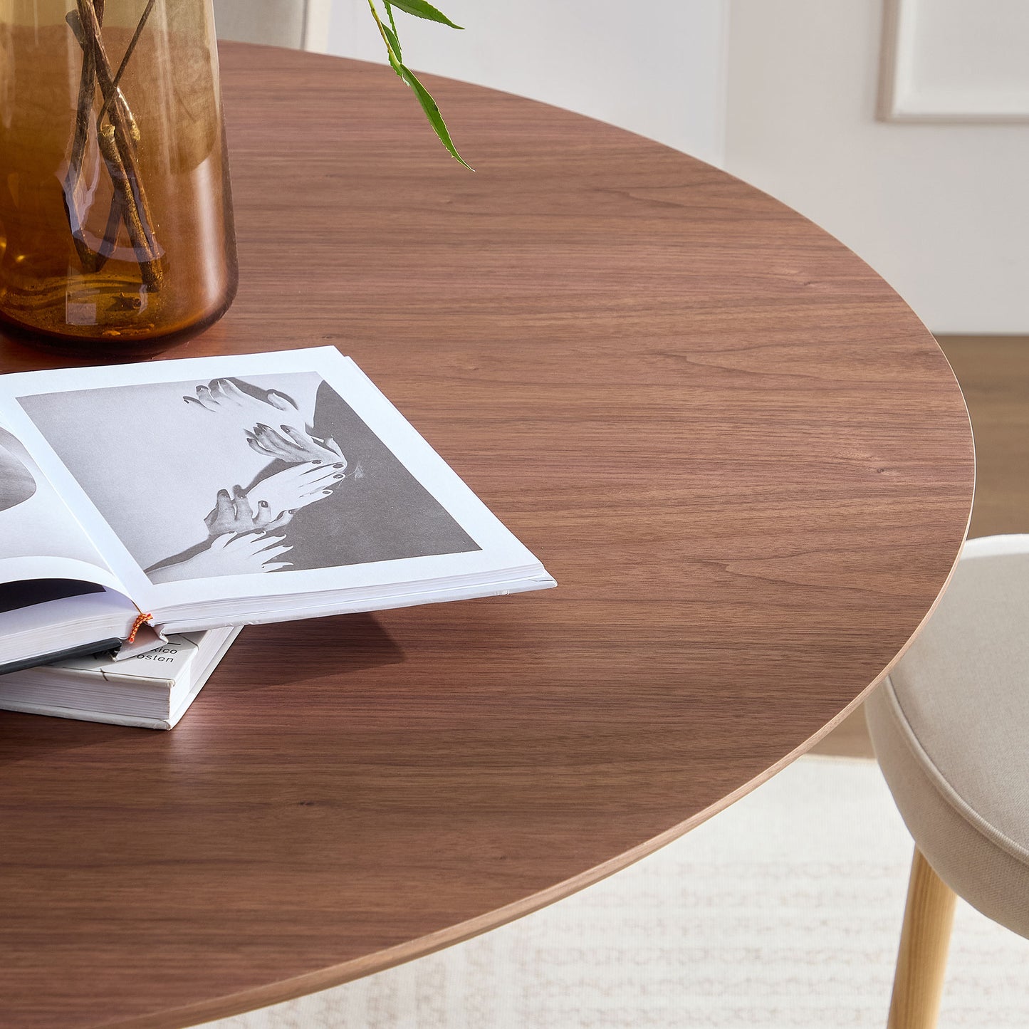 Round walnut wood dining table with open book and amber vase