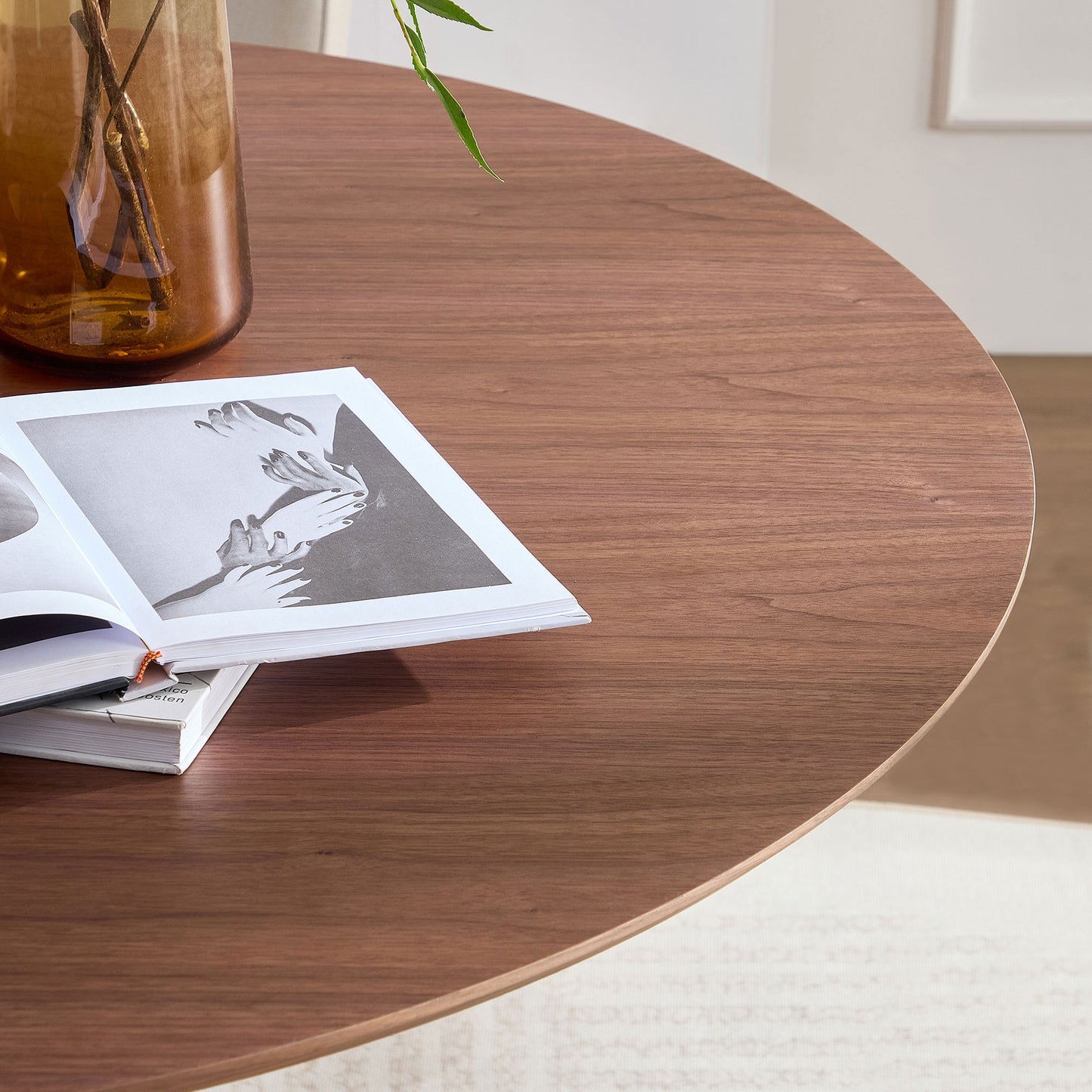 Round walnut wood dining table surface with an open book and amber vase