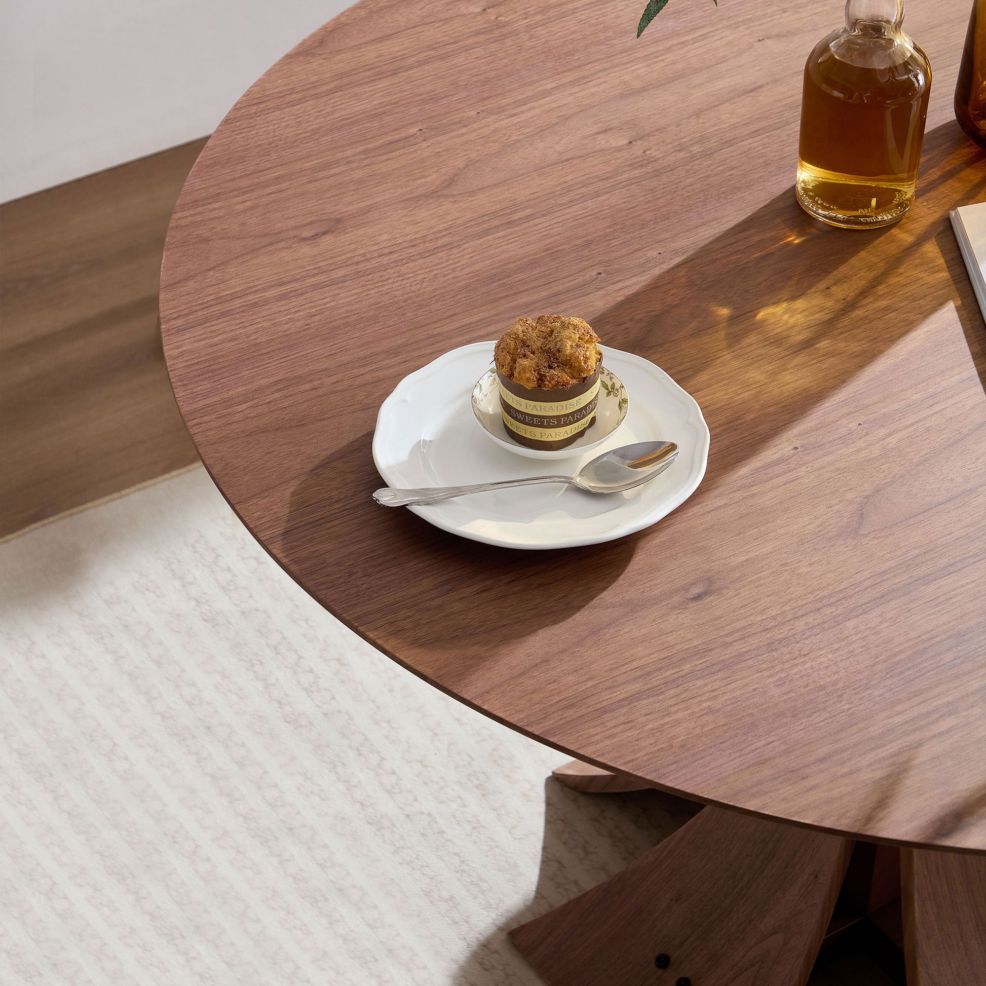 Round walnut dining table with natural wood grain and a single cupcake on a plate