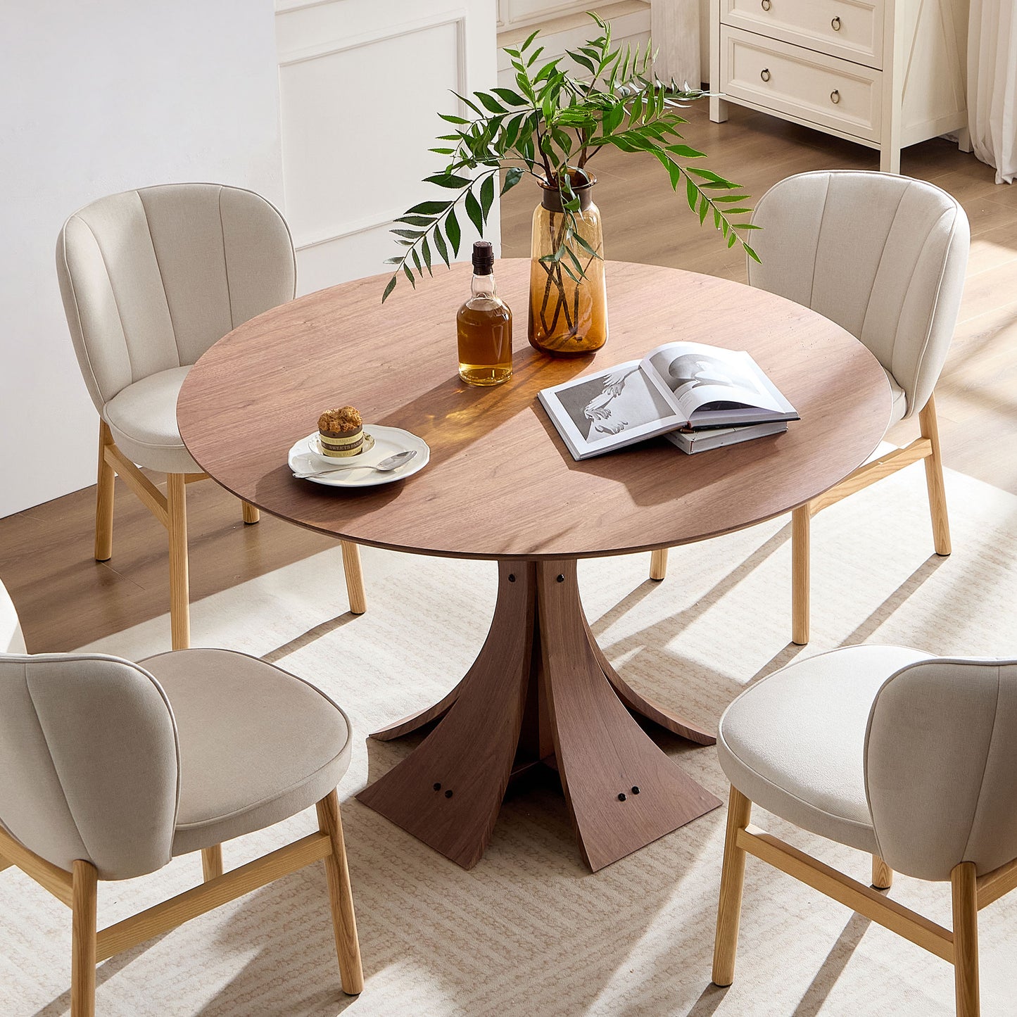 Round walnut dining table with beige upholstered chairs and modern pedestal base