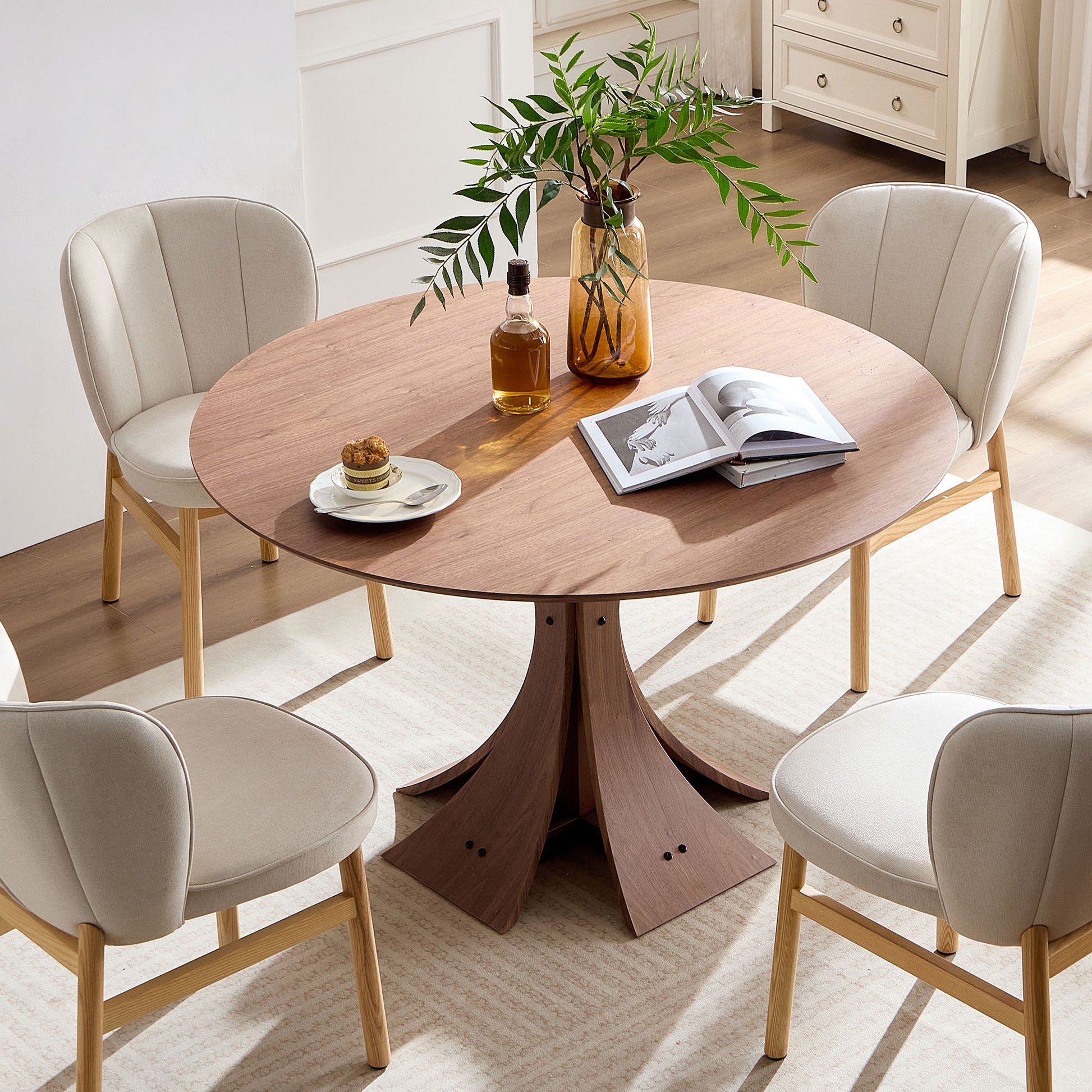 Round walnut dining table with beige upholstered chairs and modern pedestal base