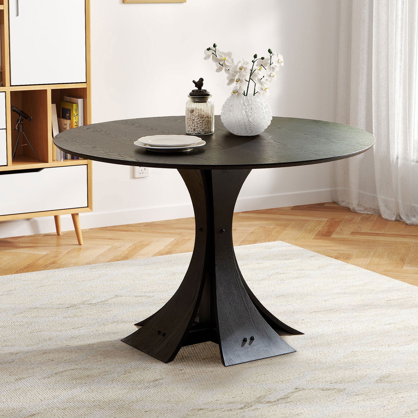 Dark wood round dining table with sculpted pedestal base and white orchid vase