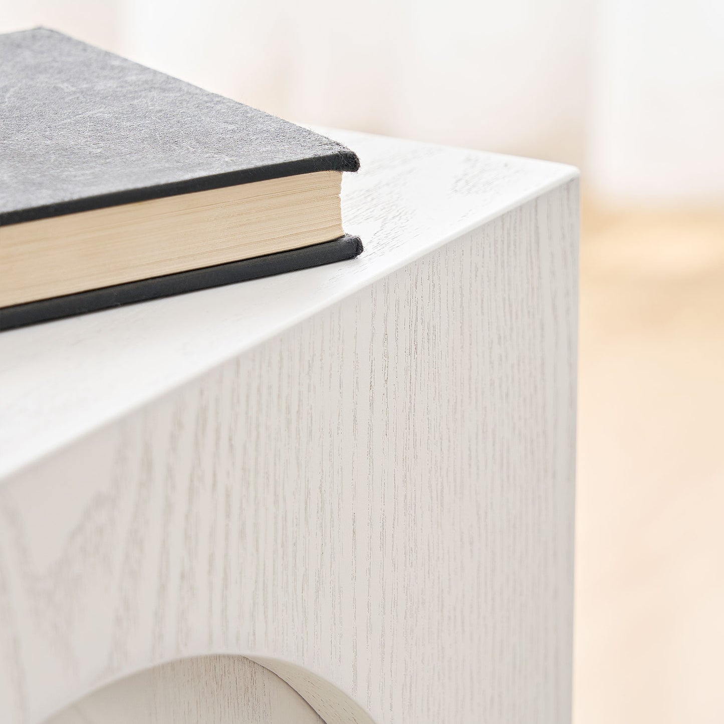 Textured black hardcover book with cream pages resting on a light woodgrain side table